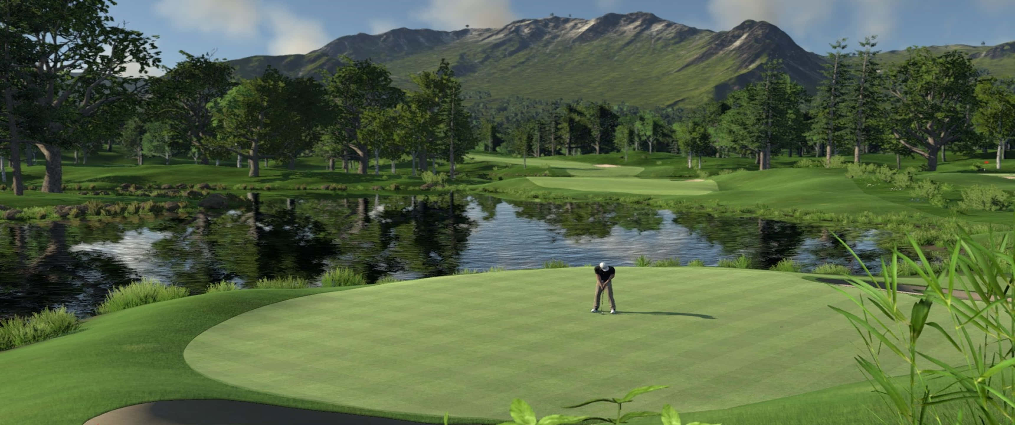 The Golf Club 3440x1440p 高爾夫球場背景 壁紙 — 一位戴黑色帽子和穿黑色襯衫的高爾夫球手在鬱鬱蔥蔥的球道上揮桿，球道兩旁是水和樹木，背景是山脈。