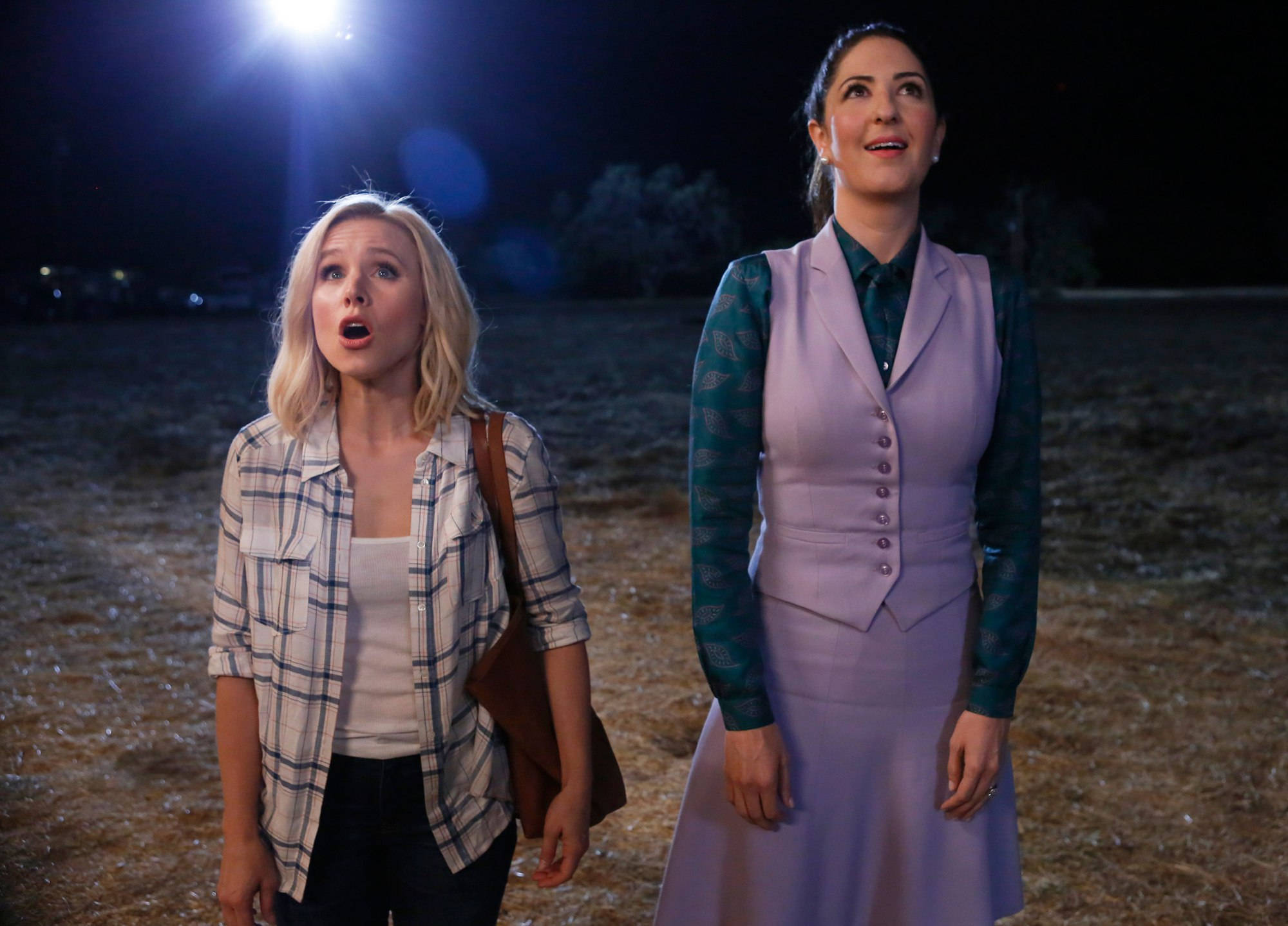 《The Good Place》愛蓮娜與珍妮特·德拉-德努奇奧 壁紙 — 兩個女人站在黑暗的田野中，在明亮的聚光燈下，張開嘴巴敬畏地仰望看不見的東西。