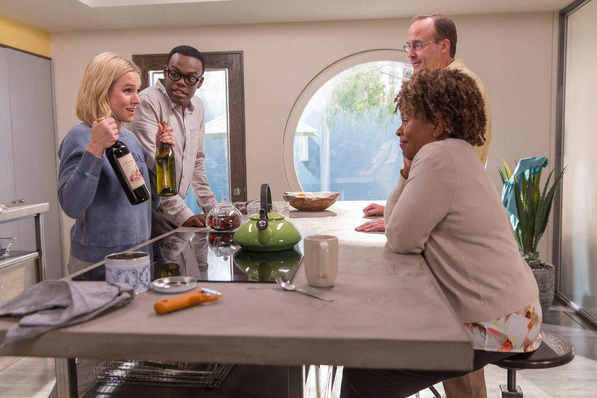 《The Good Place》角色於餐桌前準備食物 壁紙 — 四個人圍在一個現代廚房島台旁，放著酒瓶和一個綠色水壺，一邊聊天一邊大笑。