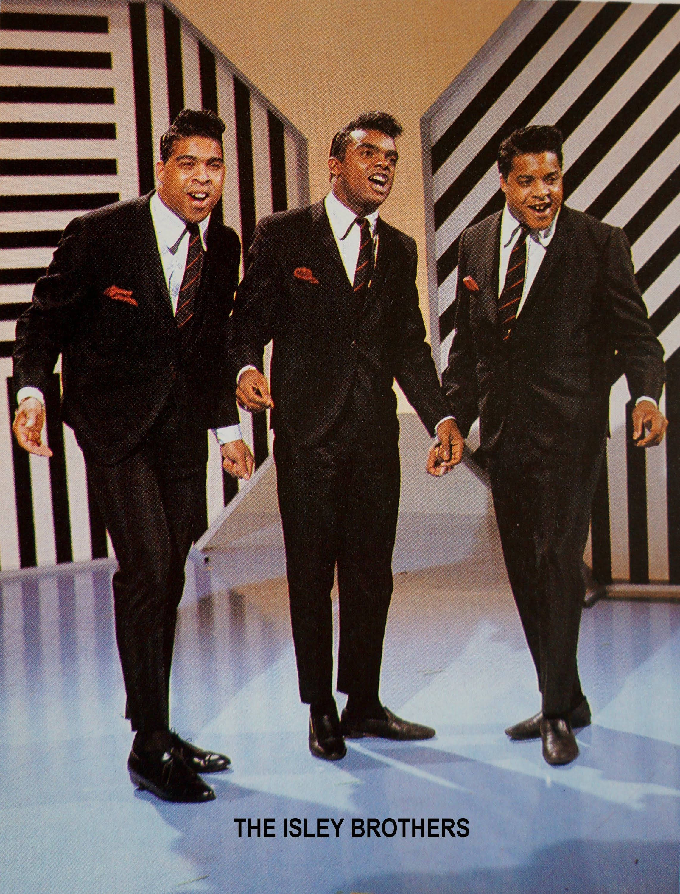 The Isley Brothers《Twist And Shout》專輯封面 壁紙 — 三位微笑的男士穿著相配的黑色西裝，口袋裡有紅色方巾，在醒目的黑白條紋背景下自信地大步走著。