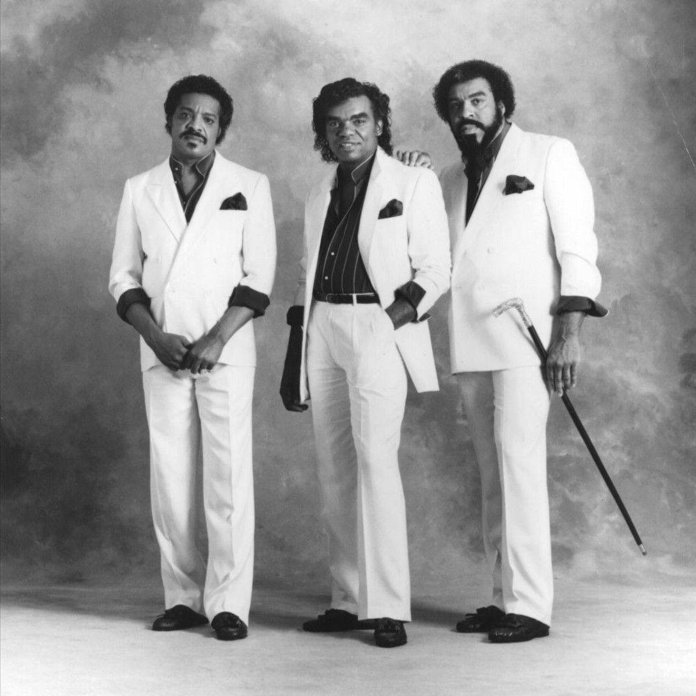 The Isley Brothers《Masterpiece》專輯封面 壁紙 — 三位時尚男士身穿白色西裝，在煙霧繚繞的攝影棚背景下，自信地擺出經典黑白肖像照的姿勢。