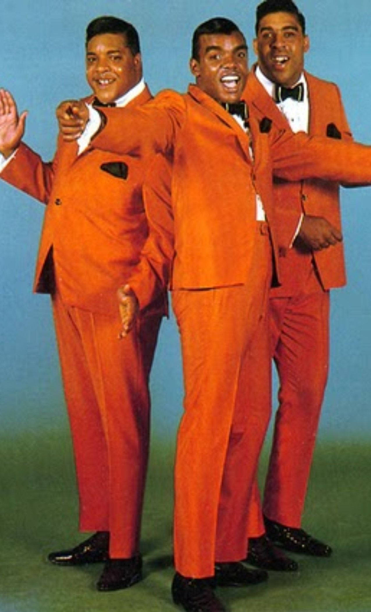 The Isley Brothers《Classic》專輯封面 壁紙 — 三位笑容滿面的男士身穿鮮豔橙色西裝，在藍綠色攝影棚背景下充滿活力地擺姿勢。