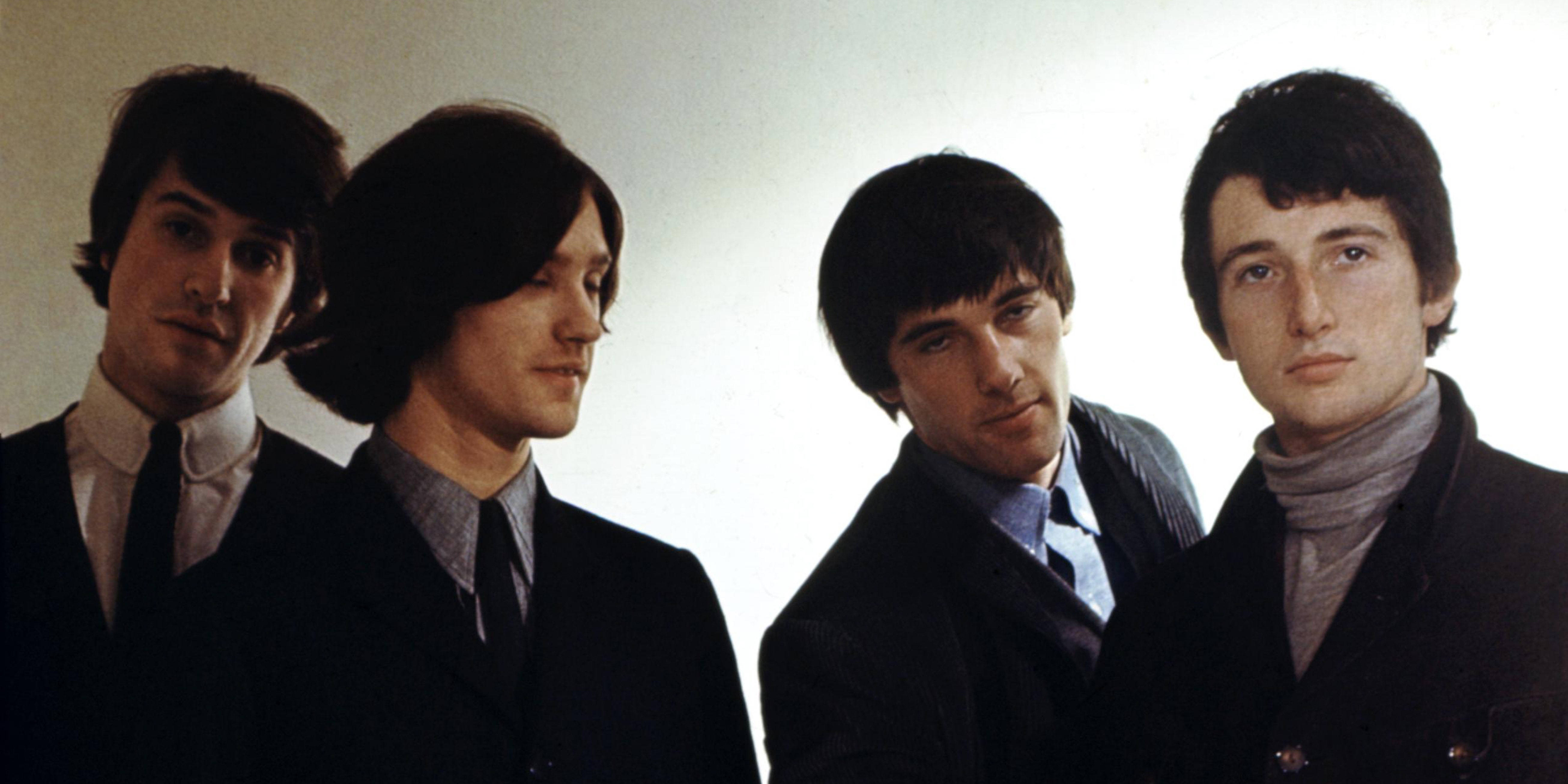 The Kinks 搞笑樂隊海報 壁紙 — 四位年輕男士身穿深色西裝和有領襯衫，在純色淺色背景前擺出嚴肅的表情。