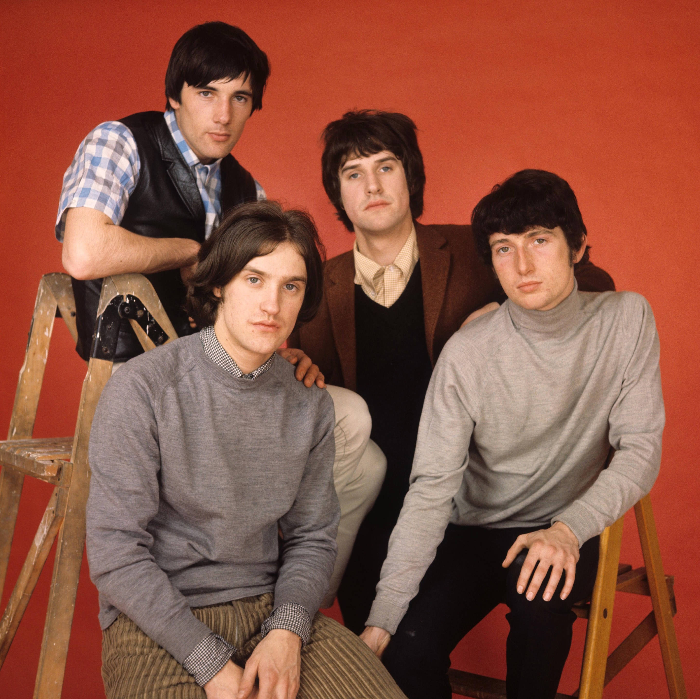 The Kinks 樂隊工作室拍攝照 壁紙 — 四位身穿1960年代服裝的男子，在純紅色背景前與木梯嚴肅地擺姿勢。