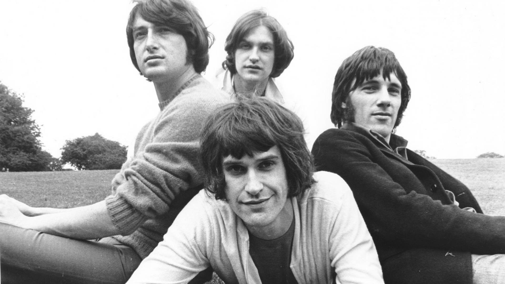 The Kinks 樂隊成員合照 壁紙 — 四位長髮男士在陰天下的草地上隨意擺姿勢，一張復古黑白照片。