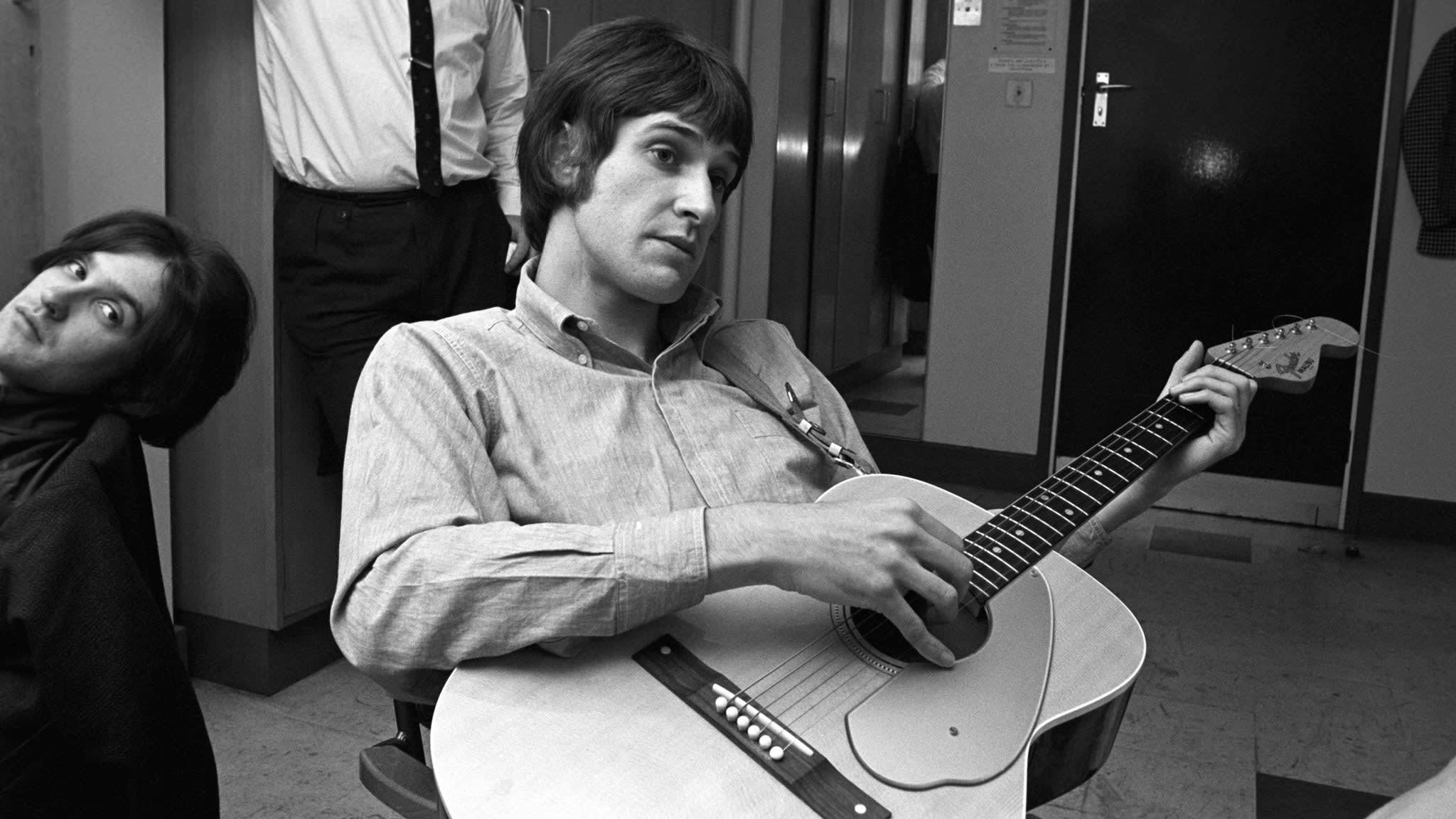 The Kinks 的 Ray Davies 舞台演出 壁紙 — 一張黑白照片，一名男子在走廊上專注地彈奏木結他，另一人則向後靠。