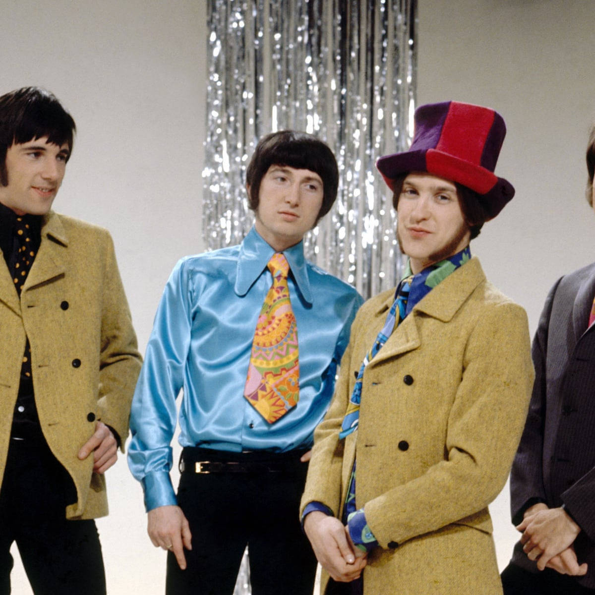 The Kinks 的時尚品味 壁紙 — 四位身穿1960年代摩登時尚的男士在閃爍的銀色簾幕背景前擺姿勢。