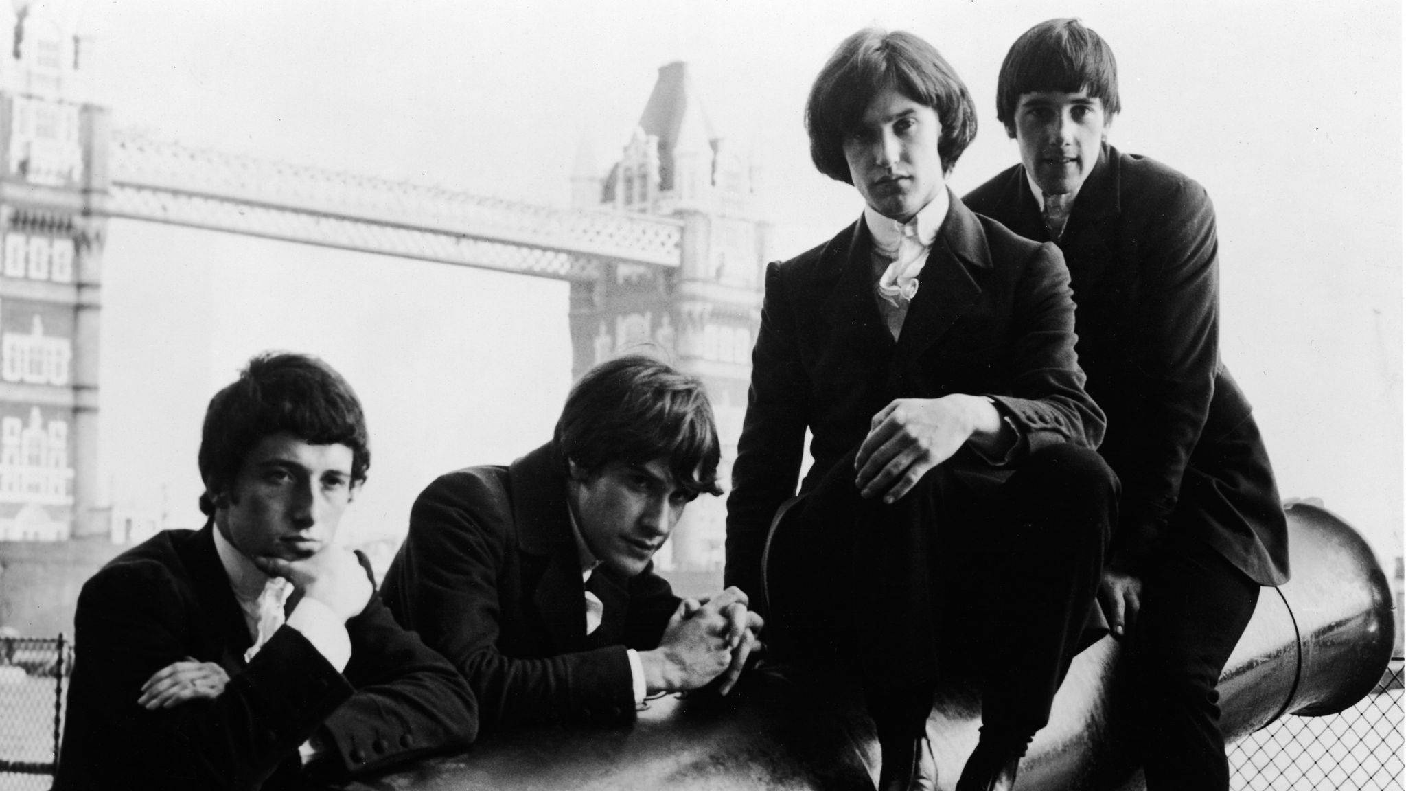 The Kinks 穿著西裝 壁紙 — 四位身穿西裝的年輕男子在屋頂上嚴肅地擺姿勢，背景可見倫敦塔橋，是一張經典的黑白照片。