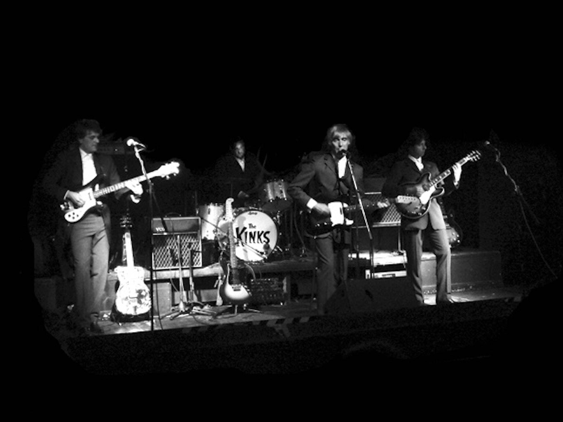 The Kinks 黑白復古海報 壁紙 — The Kinks 在昏暗聚光燈下現場表演結他和鼓的黑白照片。