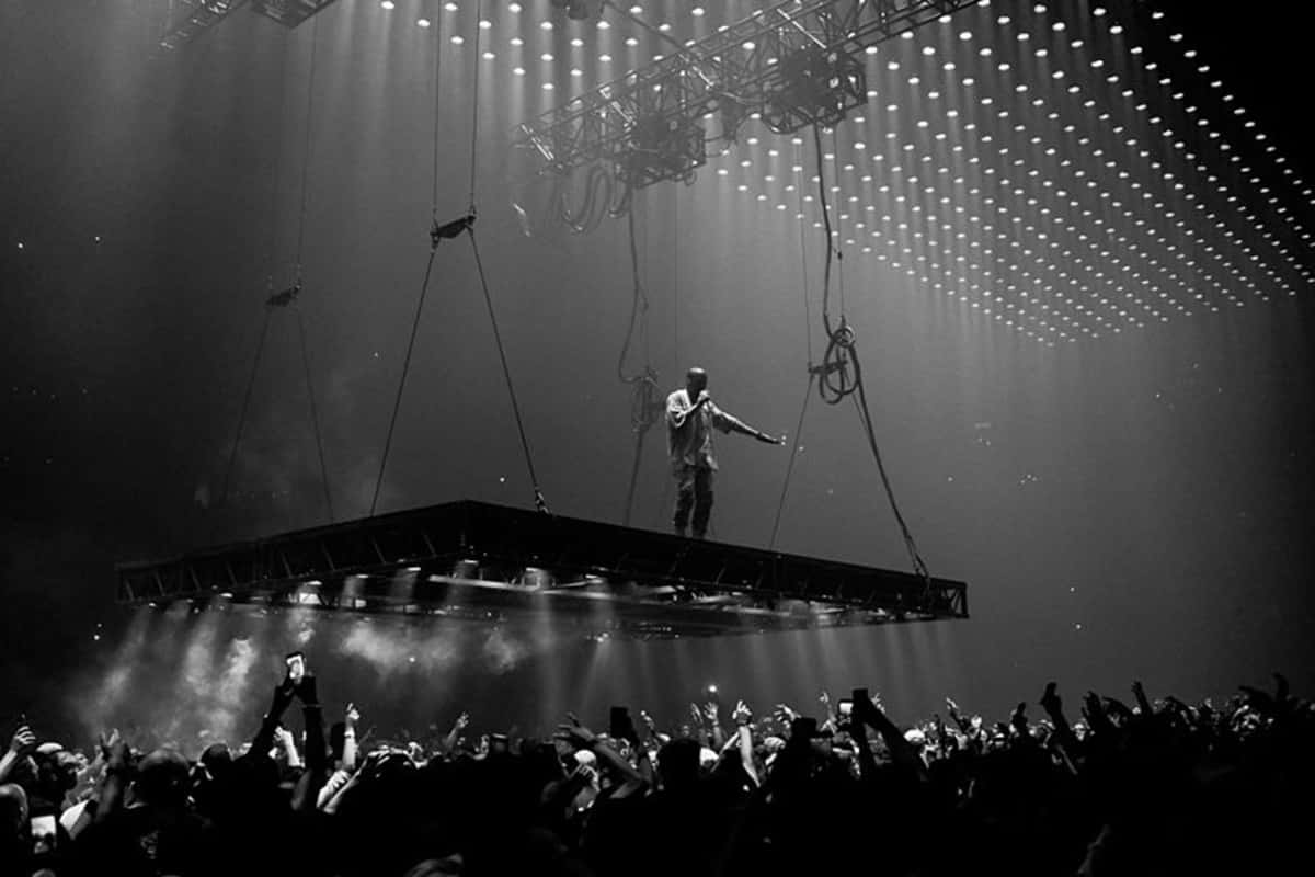 《The Life of Pablo》專輯封面：黑白經典肖像 壁紙 — 一位表演者獨自站在懸掛的舞台上，下方是喧囂的人群，上方是戲劇性的舞台燈光。