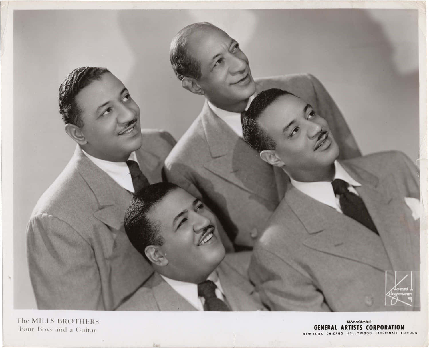 The Mills Brothers《Four Boys and a Guitar》專輯封面 壁紙 — 四位微笑的西裝男子在復古黑白工作室肖像中一起擺姿勢。