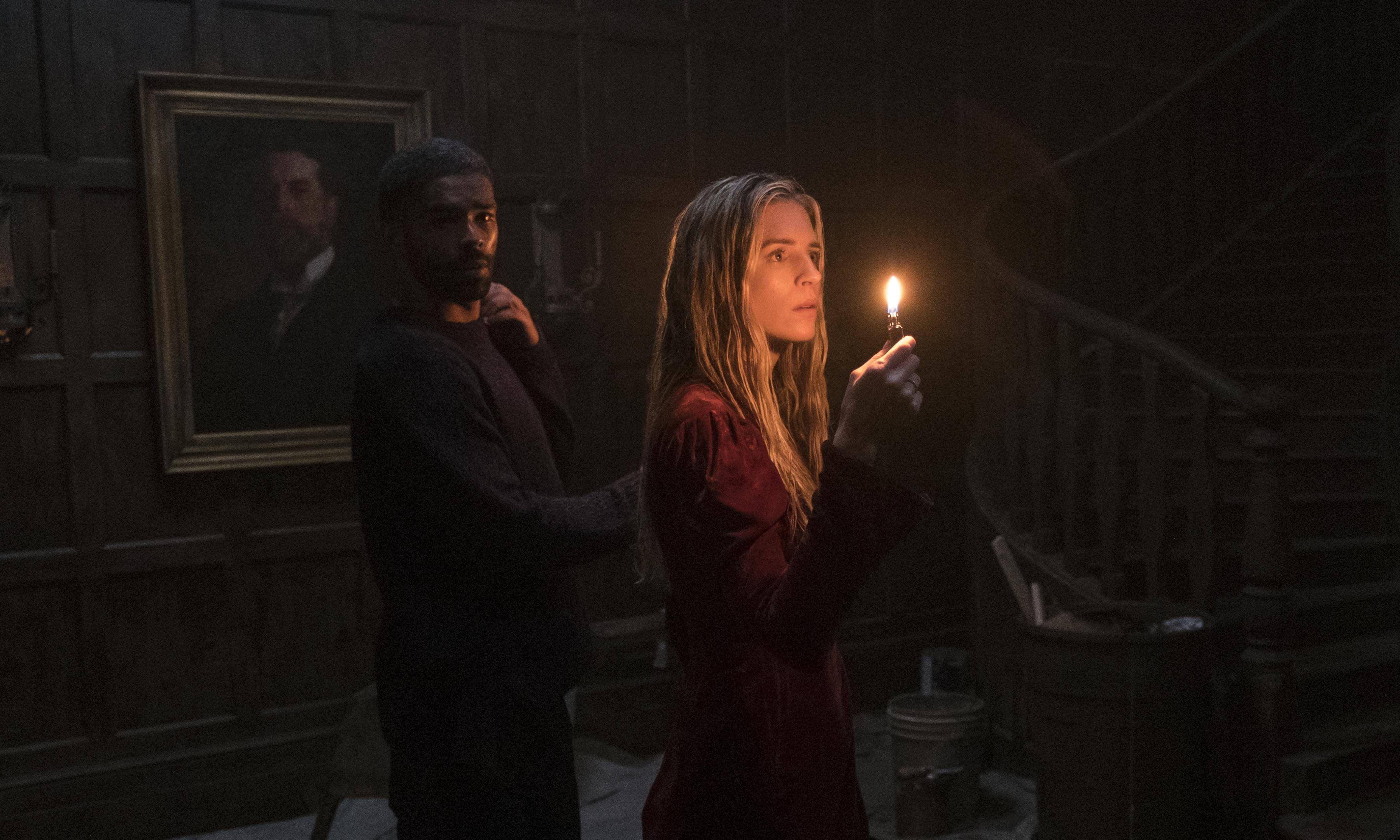 《The OA》中普萊里手持蠟燭 壁紙 — 一男一女站在昏暗的木製走廊中，手持一支閃爍的蠟燭，溫暖的光線映照在他們的臉上。
