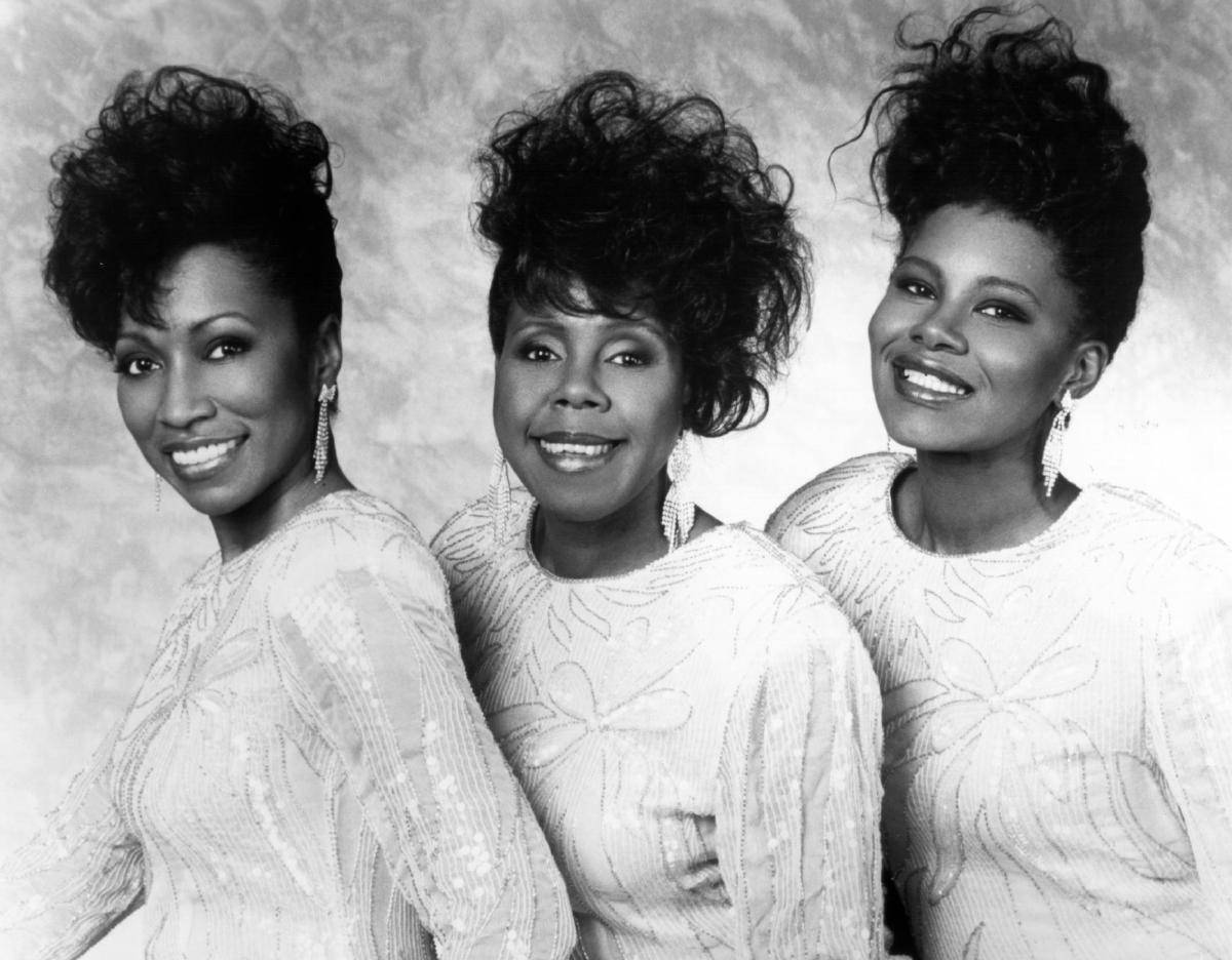The Shirelles 1989年搖滾名人堂入選儀式黑白照片 壁紙 — 三位笑容滿面、髮型豐盈的女性，穿著相配的質感上衣，在柔和的攝影棚背景前擺姿勢。