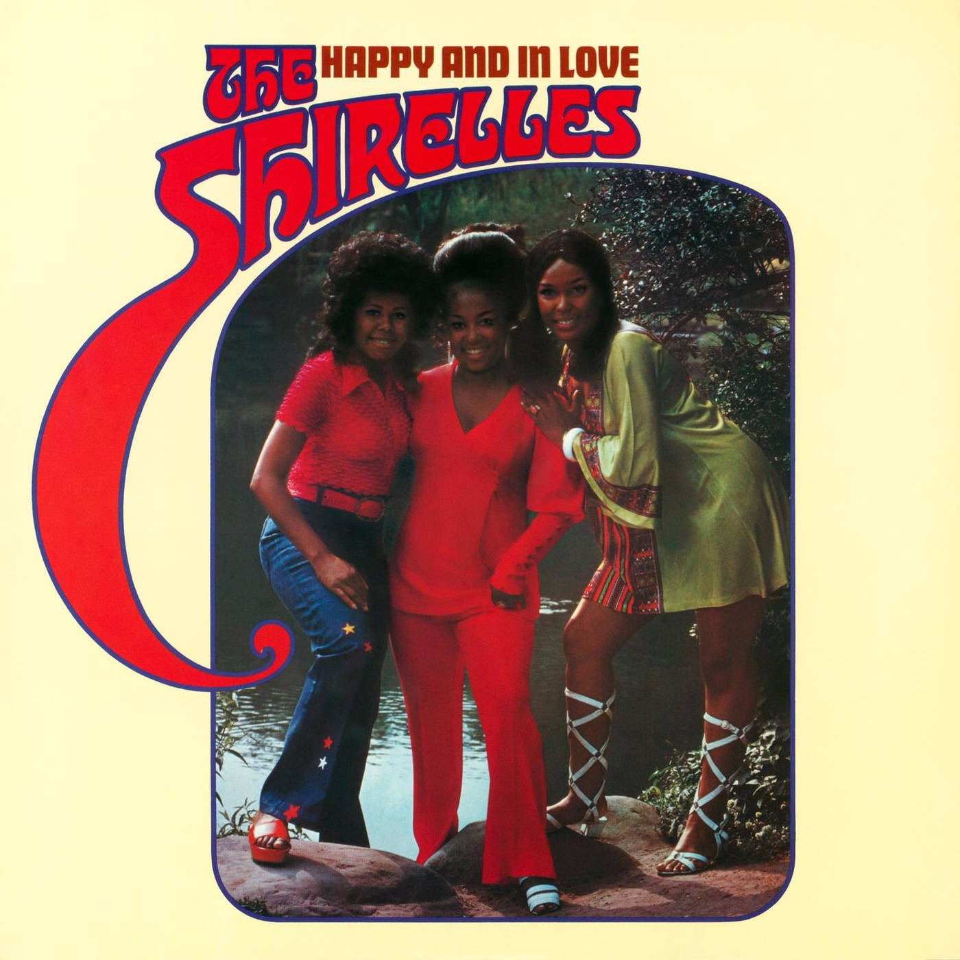 The Shirelles《Happy And In Love》1971 專輯封面 壁紙 — 三位微笑的女性穿著充滿活力的1960年代時尚，在河岸邊以奶油黃色專輯封面為背景擺姿勢。