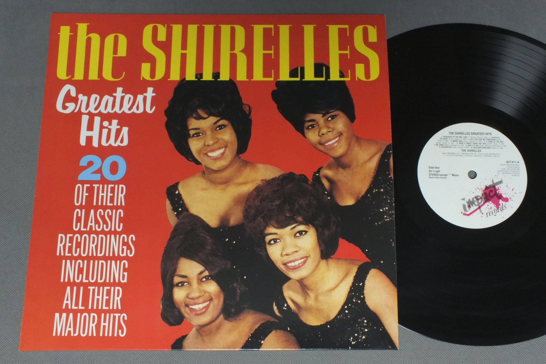 The Shirelles 最佳精選黑膠專輯 1987 壁紙 — The Shirelles Greatest Hits 的復古黑膠唱片專輯封面，四位微笑的女性穿著黑色亮片連衣裙，背景為大膽的紅色。