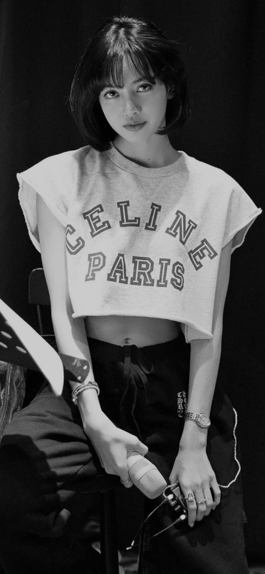 The Show彩排Lisa BLACKPINK 高畫質黑白快照 壁紙 — 一位短黑髮的年輕女性穿著Celine Paris短版衛衣，在黑色背景前手持麥克風。