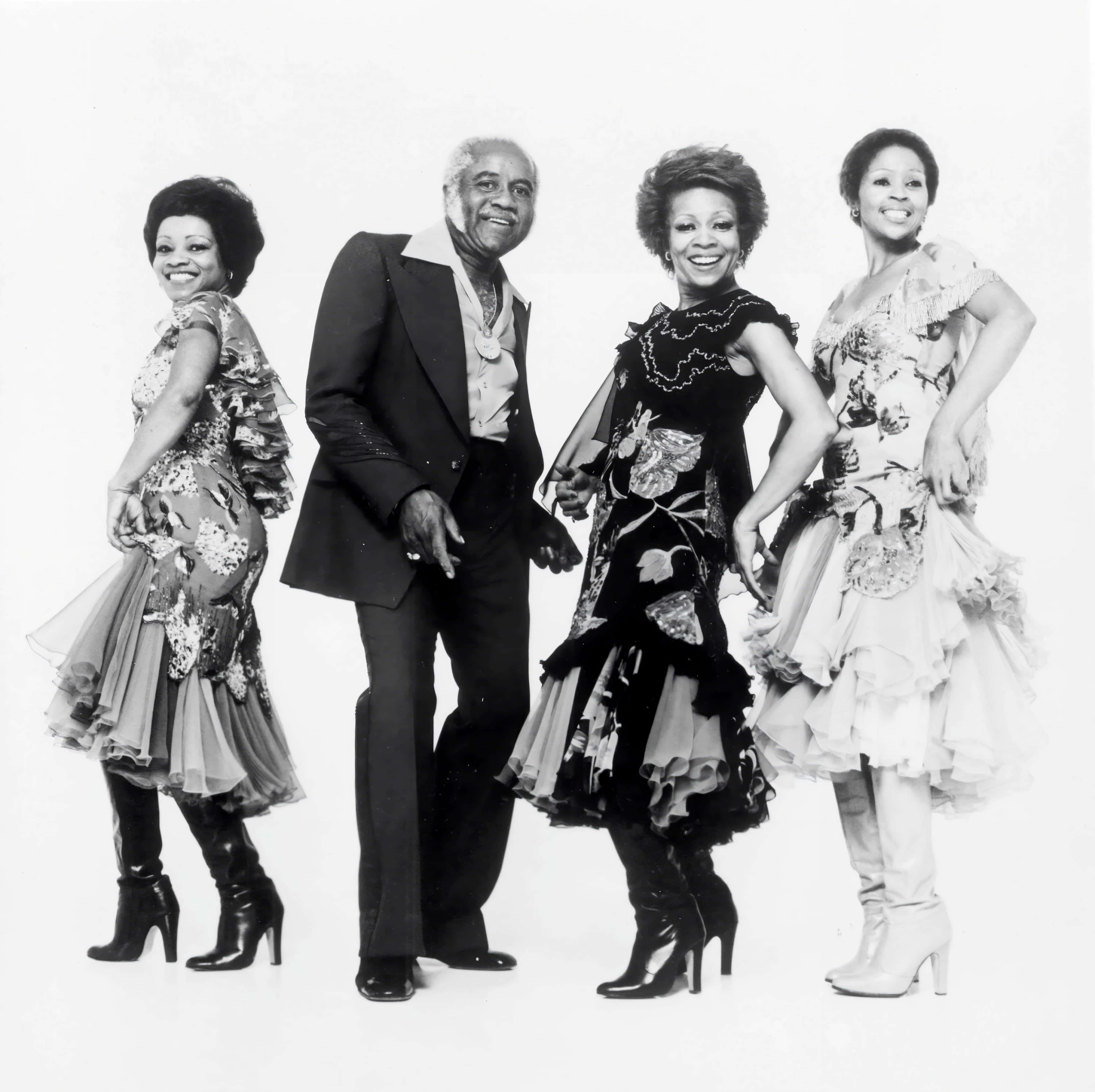 美國節奏藍調樂團The Staple Singers 1980年攝影棚拍攝 壁紙 — 四位穿著時尚的表演者自信地以純白色背景擺姿勢，拍攝經典黑白工作室肖像。