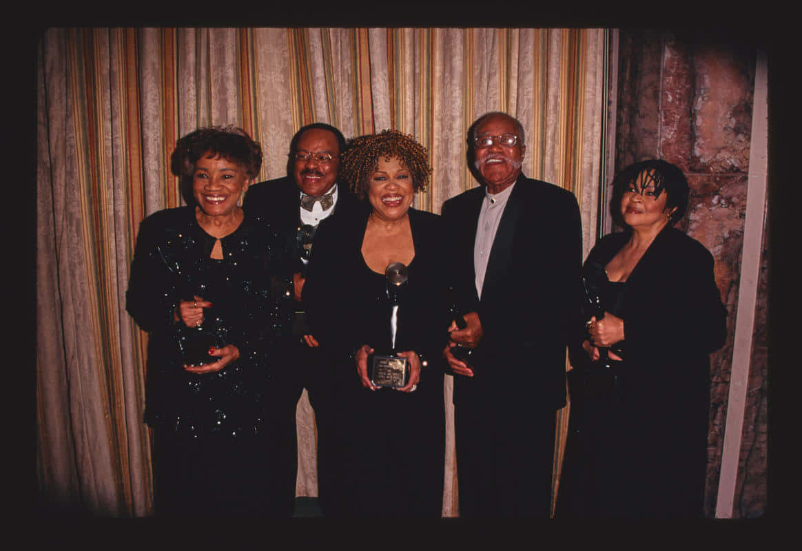 The Staple Singers 入選搖滾名人堂 壁紙 — 五位笑容滿面的得獎者身穿正裝，在條紋窗簾背景前一起手持獎盃擺姿勢。