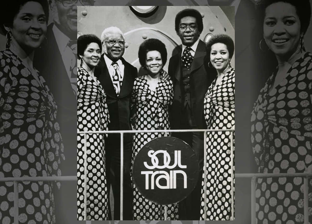The Staple Singers《Soul Train》節目合照 壁紙 — Soul Train 演員在品牌舞台前微笑的黑白照片，穿著圓點連衣裙和西裝。