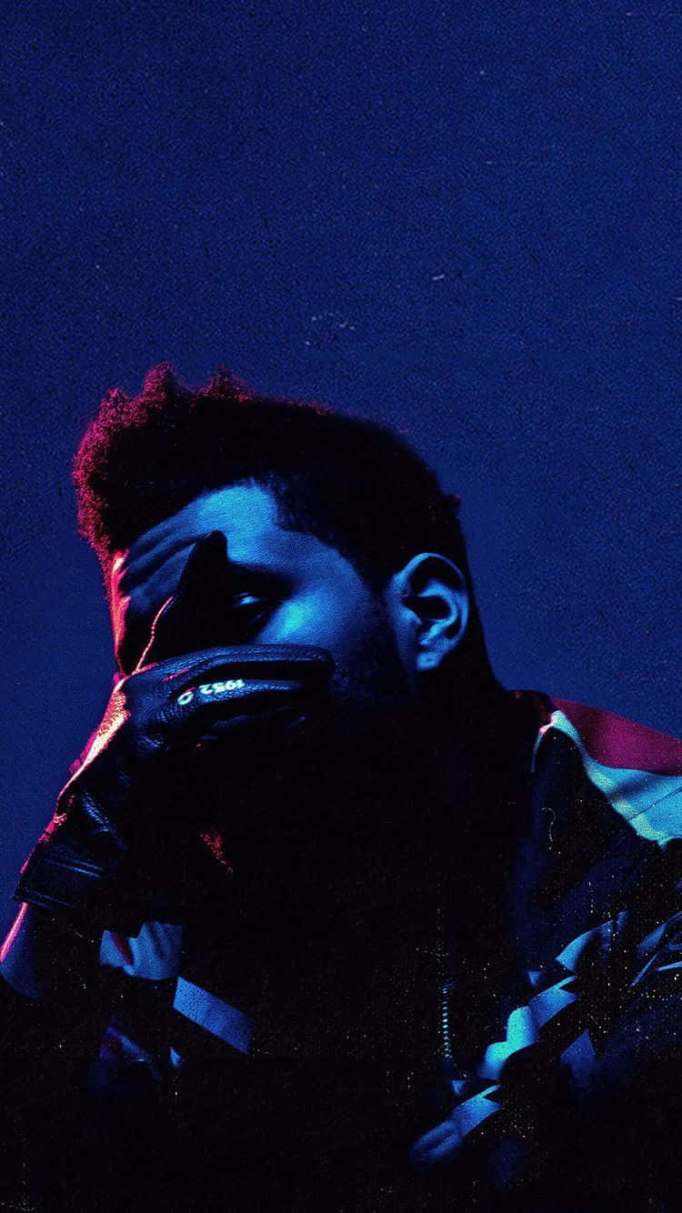 立即擁有最新 The Weeknd 主題 iPhone！現已上市！ 壁紙 — 一個穿著深色外套和手套的男人，在帶有微妙星星的深藍色夜空下捂住嘴巴。