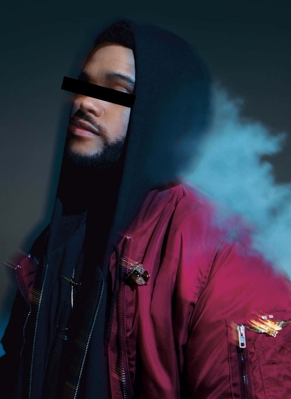 The Weeknd iPhone 壁紙 - 豐彩奪目 壁紙 — 一個穿著黑色連帽衫和紅色外套的男人在黑暗、氣氛濃厚的背景下，伴隨著戲劇性的燈光呼出煙霧。