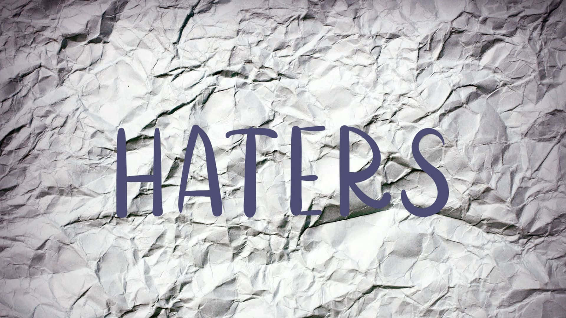  壁紙 — 粗體紫色字母的「haters」一詞在帶有紋理的皺巴巴白色紙張背景上顯得格外突出。