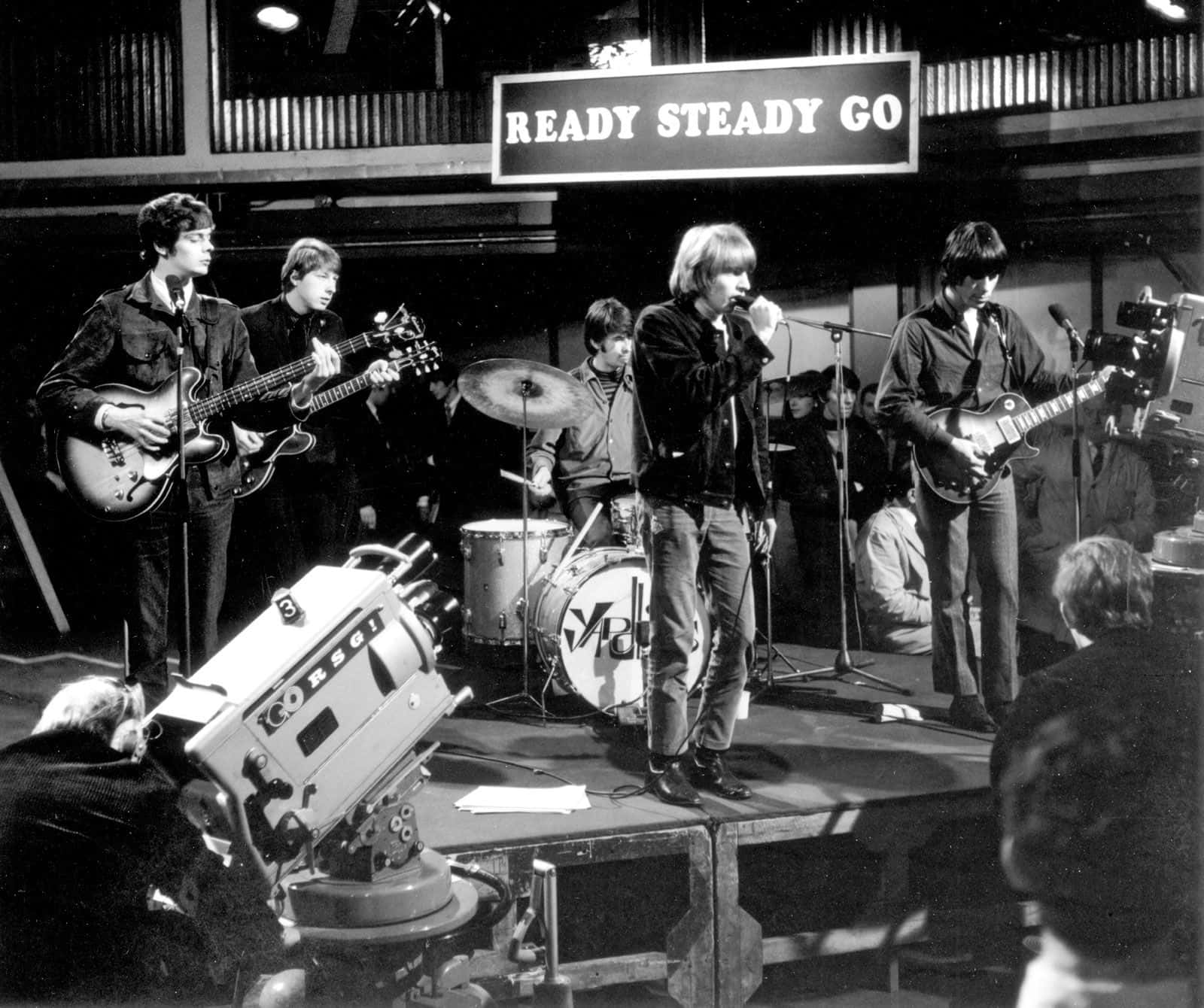 The Yardbirds 1960 年代搖滾樂隊黑白演出照 壁紙 — 一張黑白照片，拍攝了一支樂隊在電視台錄影廠舞台上，在「READY STEADY GO」標誌下現場表演。