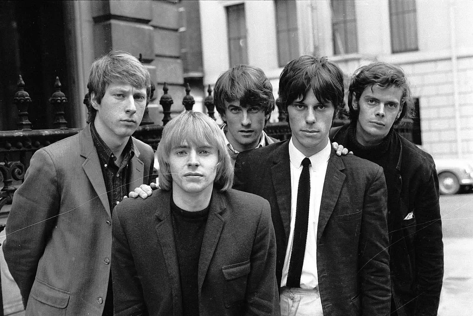 The Yardbirds — 搖滾音樂先驅 壁紙 — 五位身穿西裝的年輕男子在戶外莊嚴地站在一座帶有華麗欄杆的建築物前，這是一張復古黑白照片。