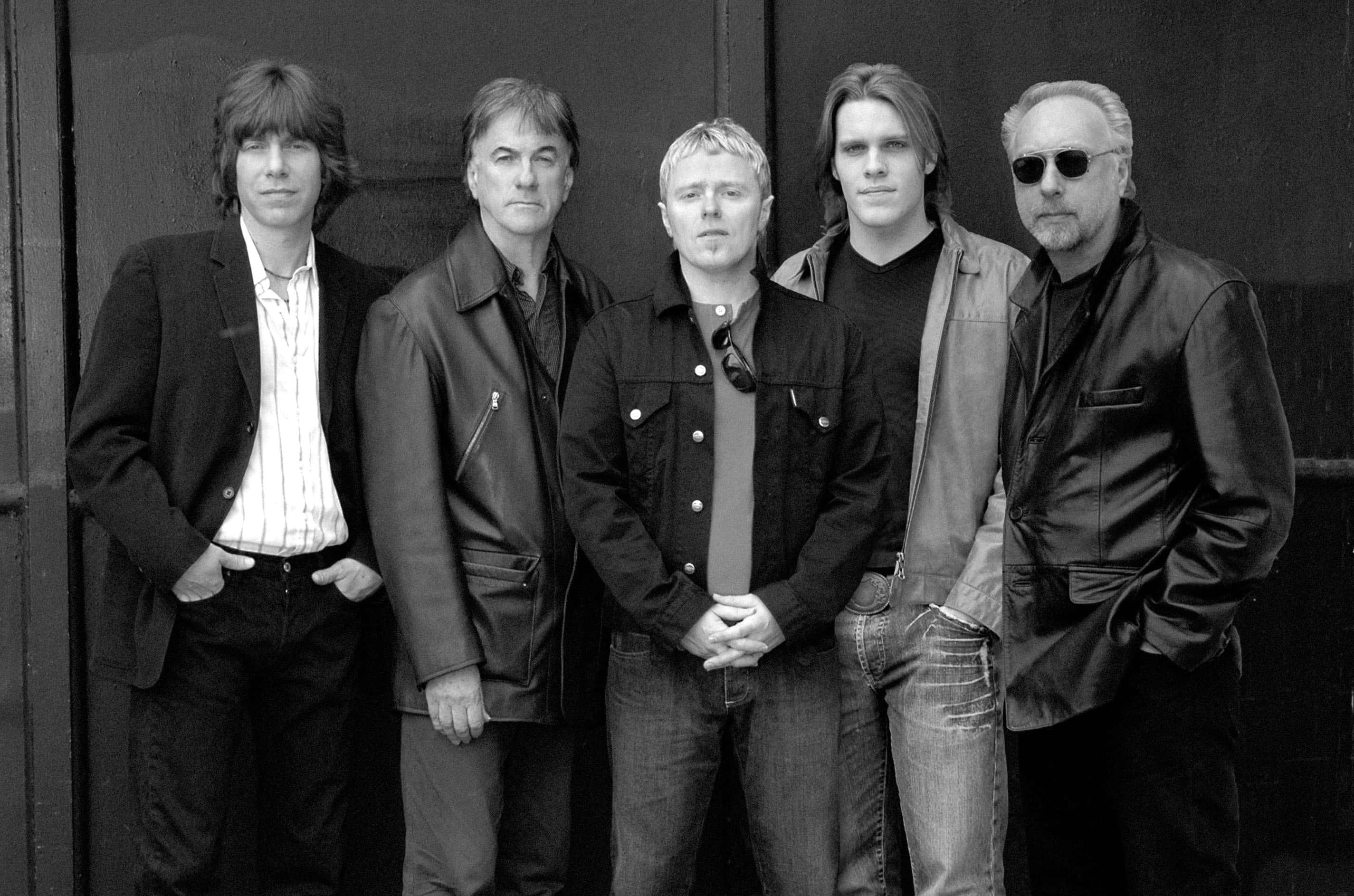 The Yardbirds 樂隊成員黑白影像 壁紙 — 五個身穿外套和牛仔褲的男人自信地站在深色紋理牆前，呈現出鮮明的黑白肖像。