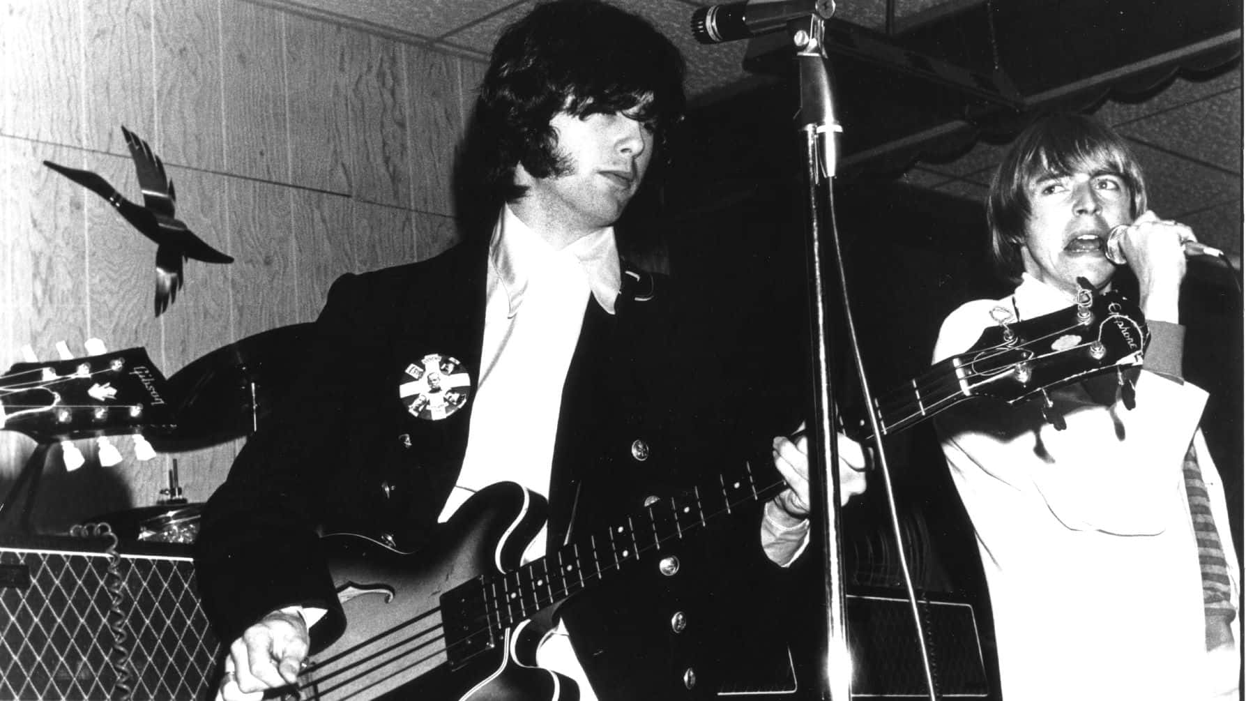 The Yardbirds 的傳奇樂手吉米·佩奇與基思·雷爾在巔峰時期的經典影像 壁紙 — 兩位音樂家在木鑲板牆前以黑白風格現場表演，手持結他和麥克風。