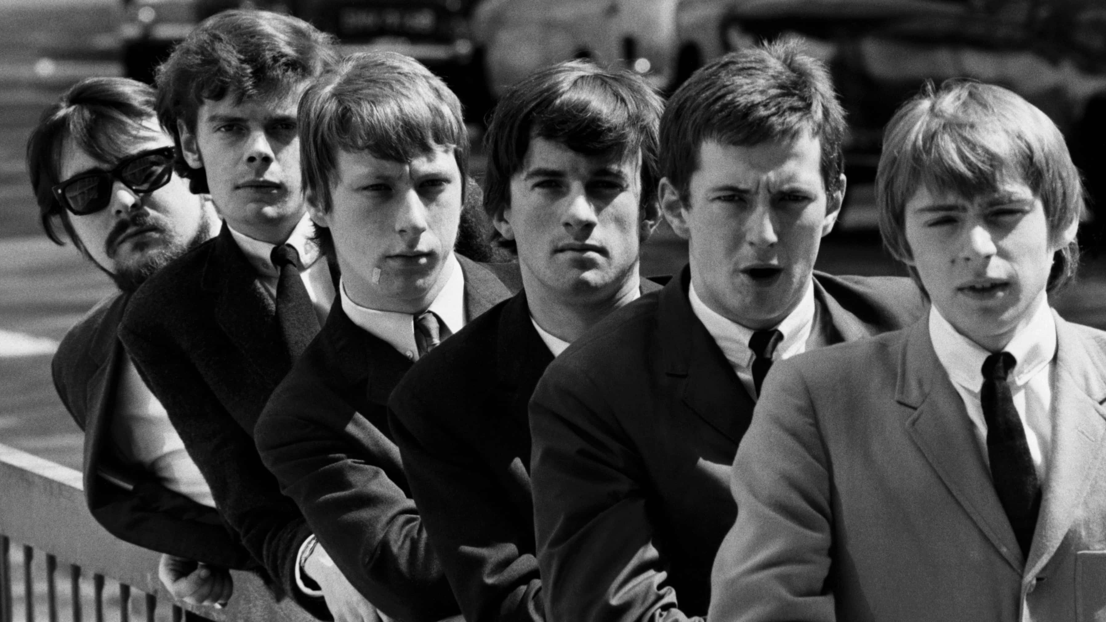 The Yardbirds — 英國搖滾先驅 壁紙 — 六位身穿西裝的年輕男子在復古黑白照片中，表情嚴肅地靠在欄杆上。