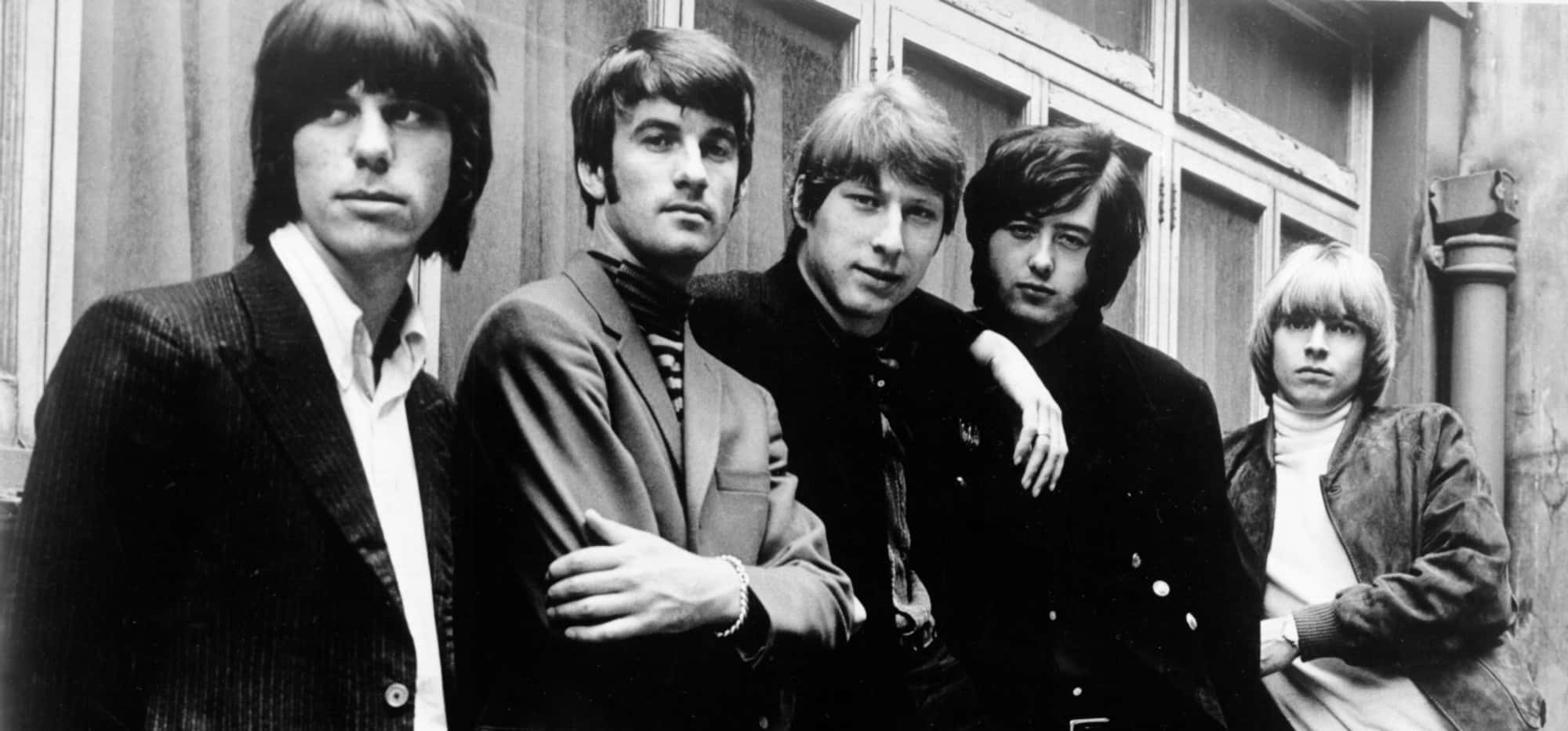 The Yardbirds黑白影像 壁紙 — 五位身穿1960年代西裝和髮型的年輕男子，在黑白照片中嚴肅地站在有窗的建築物外牆前。