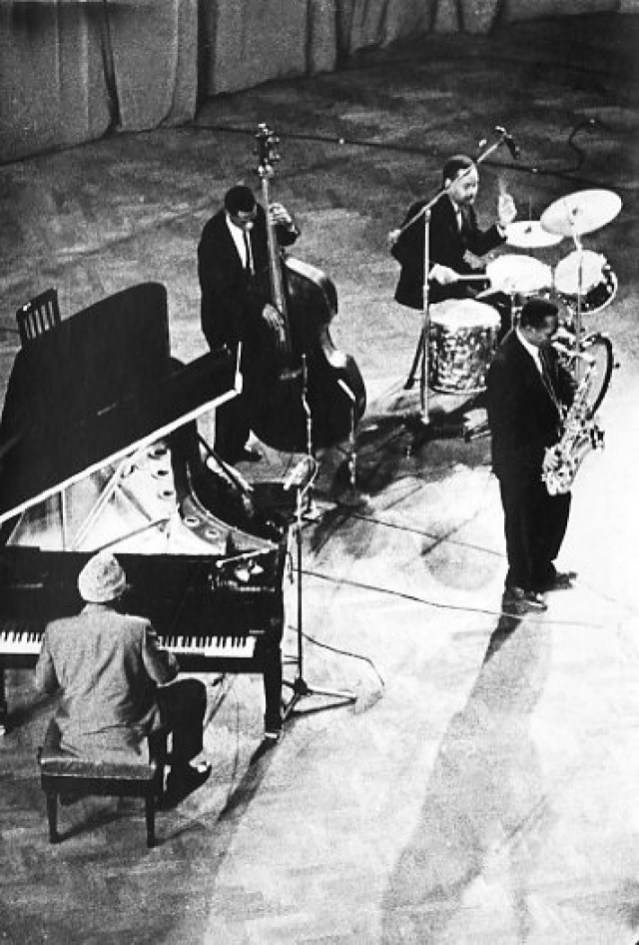 Thelonious Monk 與 Eddie Gomez 演出 壁紙 — 一張黑白照片捕捉到一個爵士四重奏在昏暗的舞台上表演，包括鋼琴手、低音提琴手、鼓手和色士風手，身穿正式服裝。