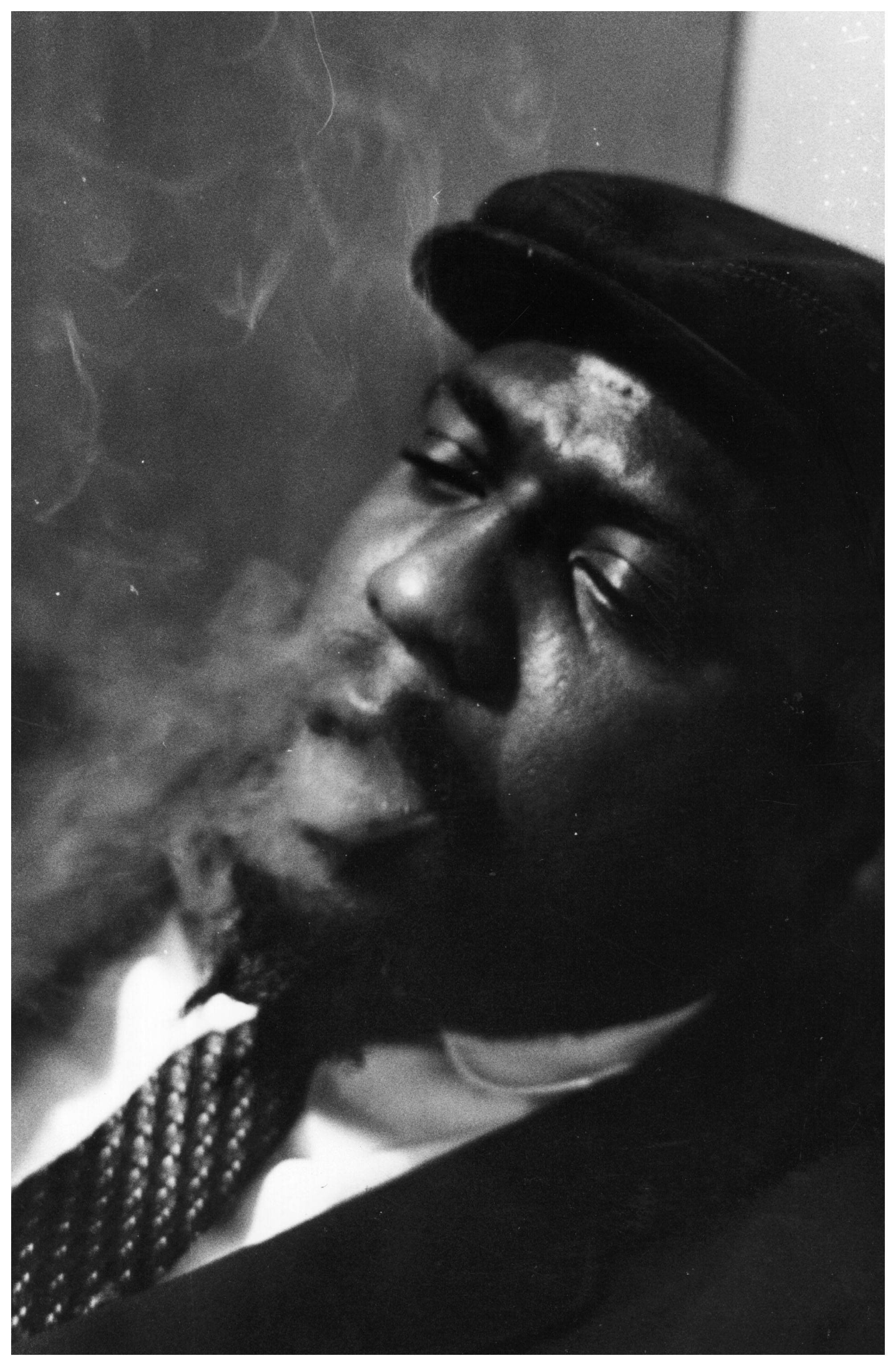 Thelonious Monk 沉浸於深邃旋律 壁紙 — 一個戴帽子的男人在黑白肖像中呼出煙霧，表情沉思。