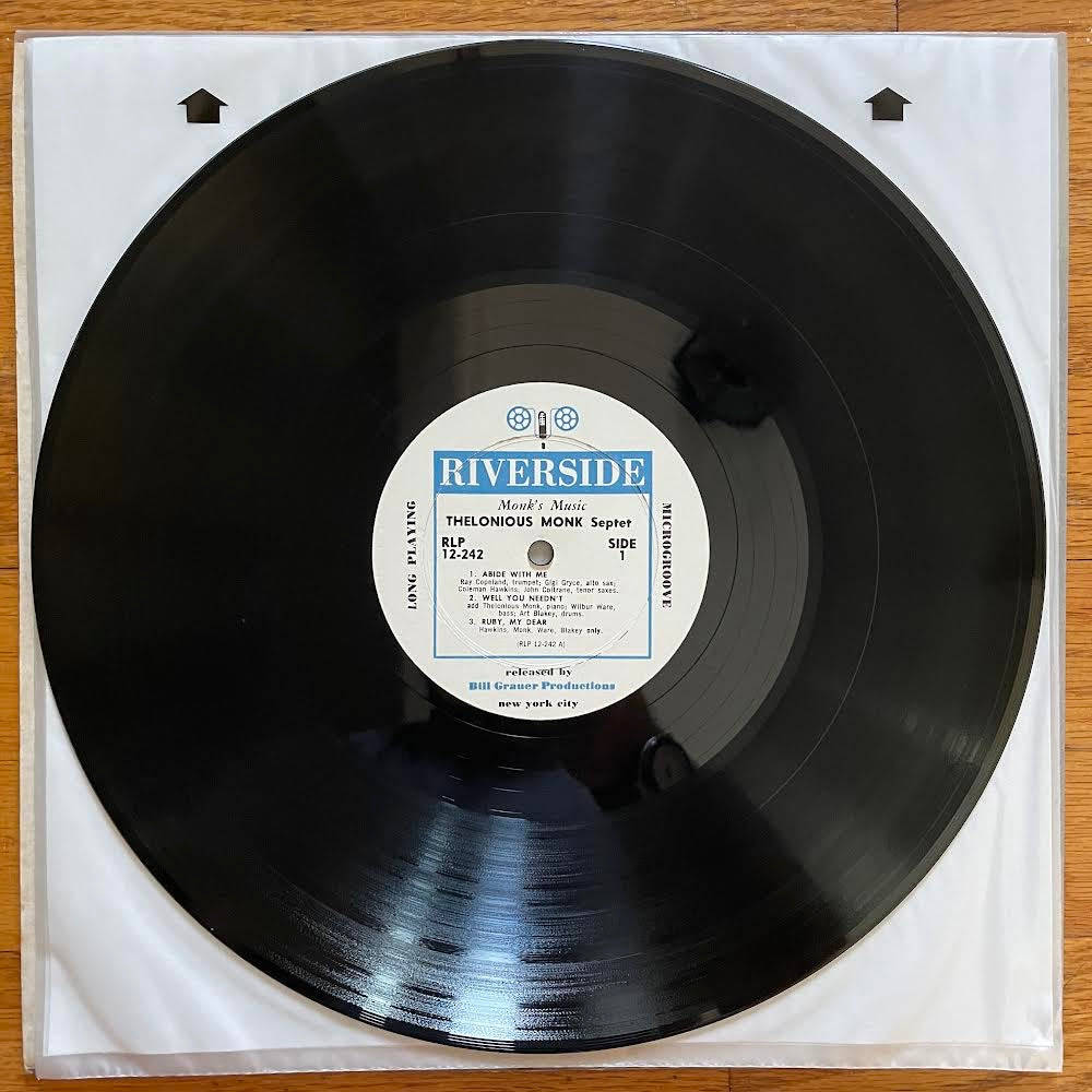Thelonious Monk Riverside 黑膠唱片 壁紙 — 一張黑色黑膠唱片，白色標籤上寫著「Riverside Thelonious Monk Septet」，放在白色封套內，置於木質表面上。