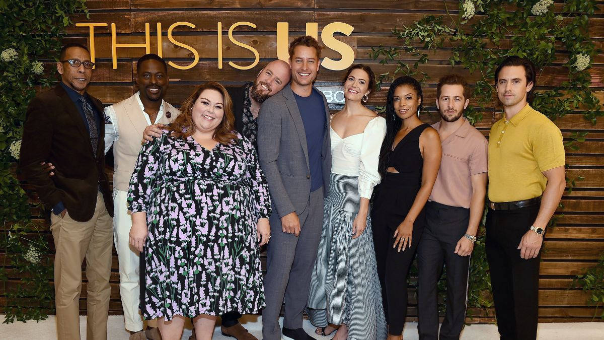 《This Is US》NBC活動現場 壁紙 — 《This Is Us》嘅演員喺有綠色植物同節目名標牌嘅木牆前面微笑擺甫士。