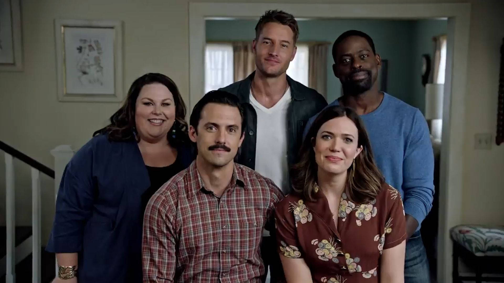 《This Is US》佩森家族 壁紙 — 五個微笑的人一起在溫暖照明的家居走廊中擺姿勢，身後可見裱框藝術品和樓梯。
