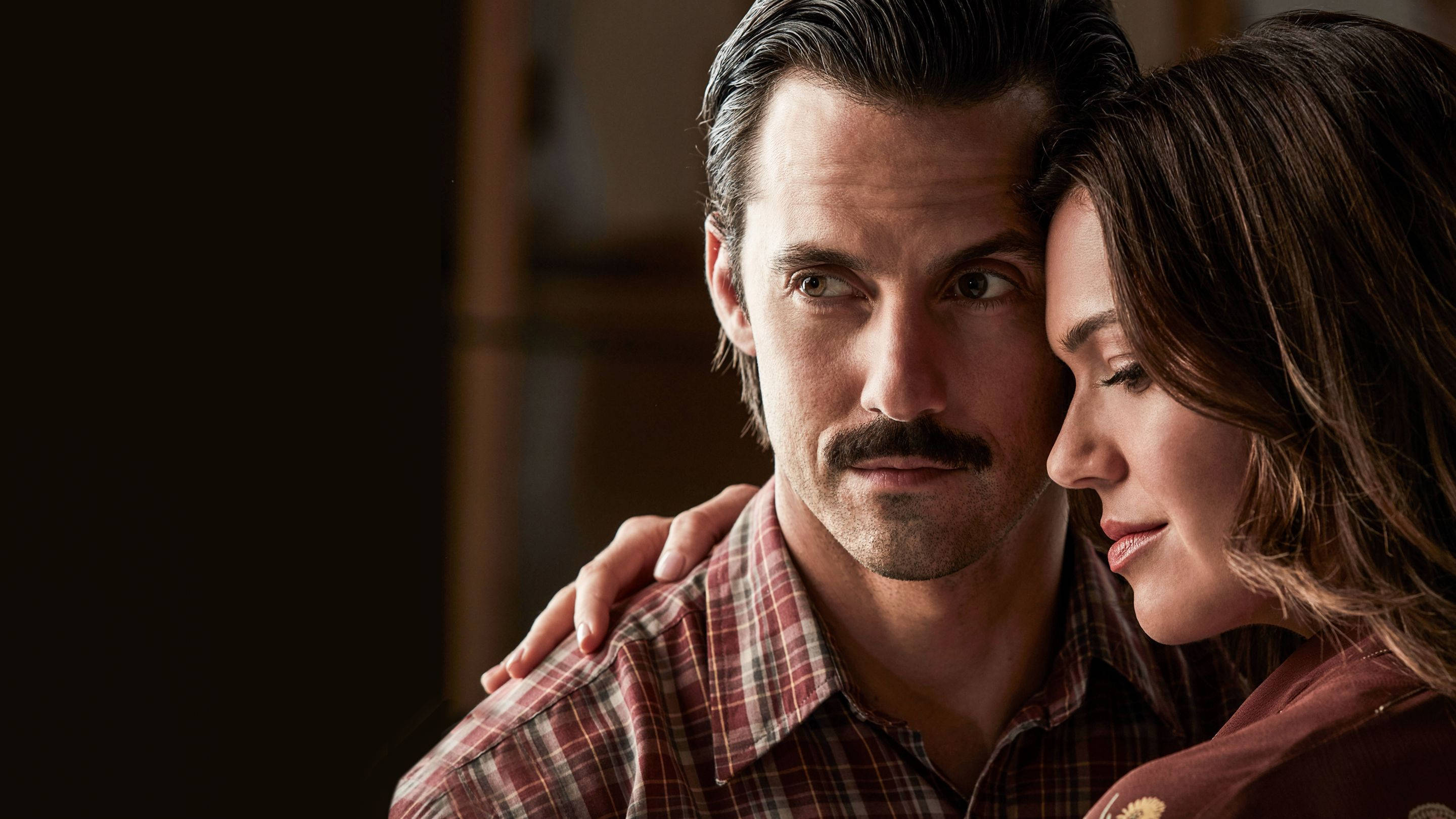 《This Is US》傑克與麗貝卡 壁紙 — 一位留鬍子的男士和一位穿著格仔衫的女士在室內溫暖燈光下分享親密時刻。