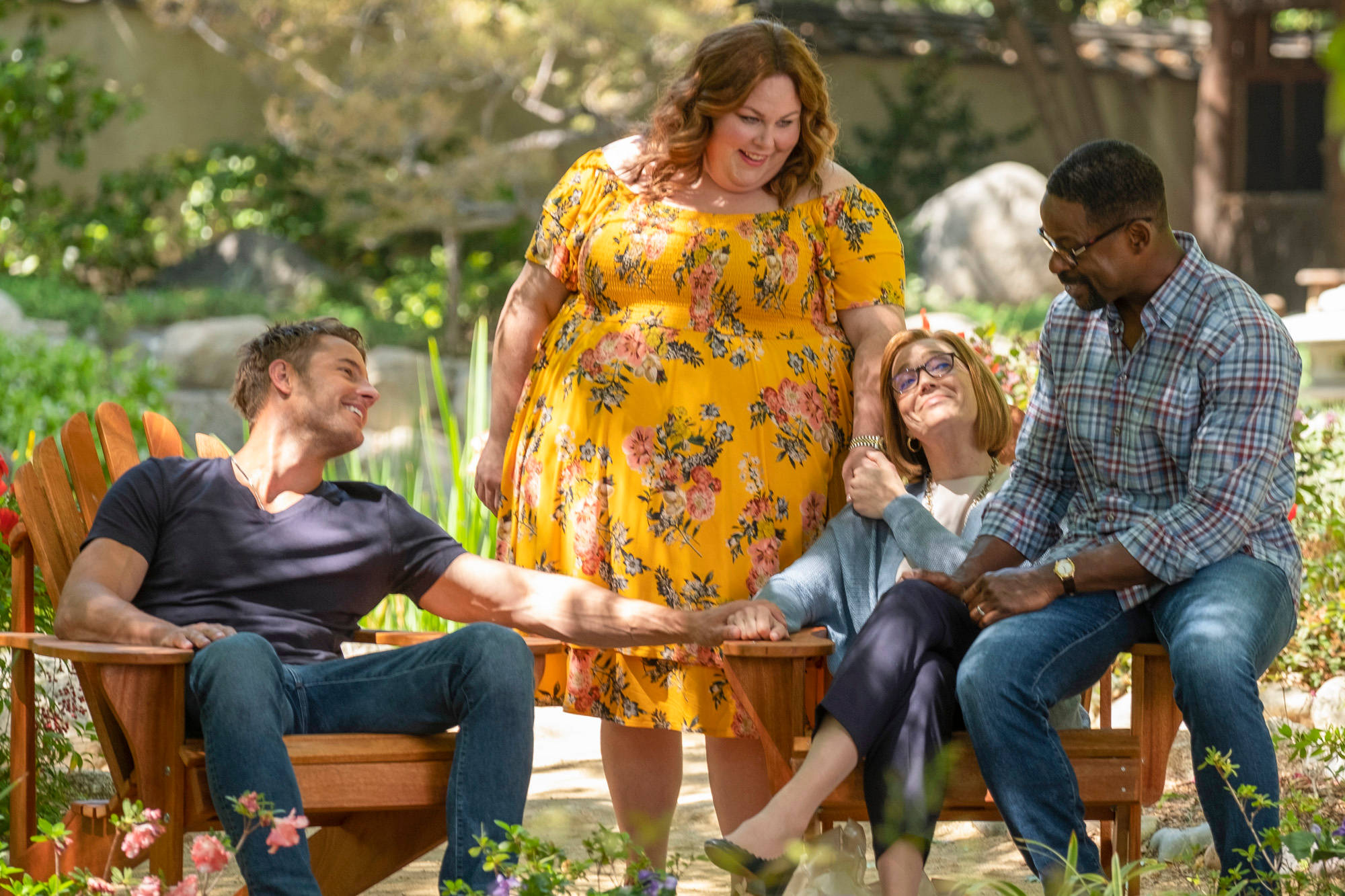 《This Is US》第六季劇組 壁紙 — 四位微笑的成年人分享溫暖的花園時光，在斑駁的陽光下手牽手坐在木椅上。