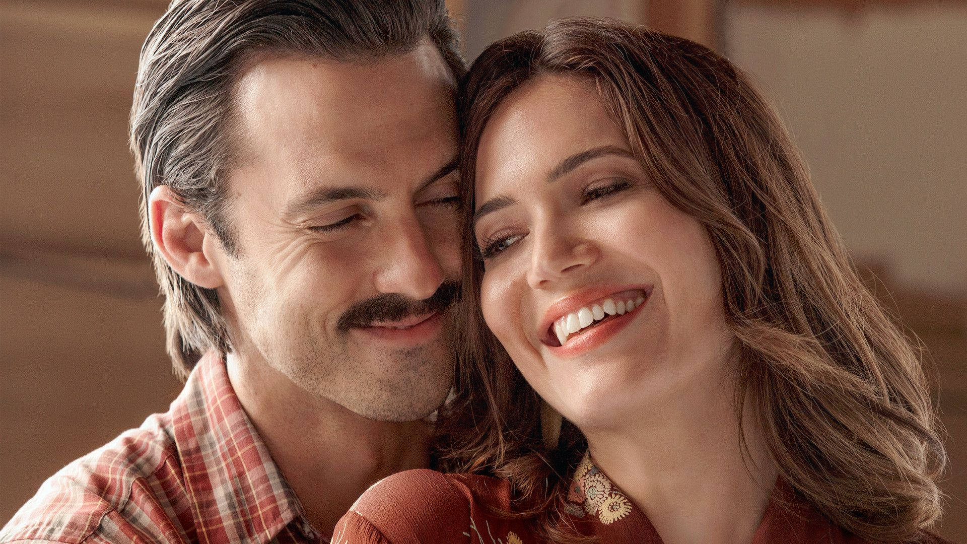 《This Is US》米洛與曼迪 壁紙 — 一對微笑的情侶在溫暖燈光和柔和焦點背景下分享溫馨時刻。