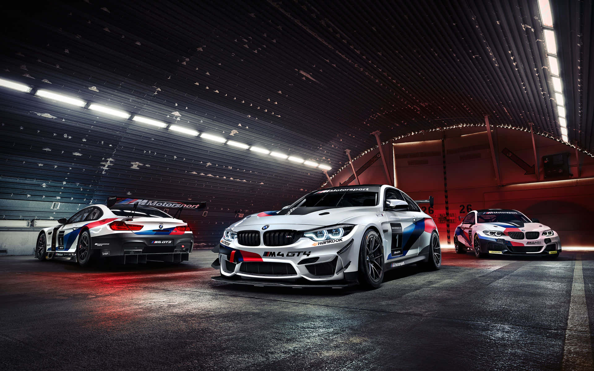 三輛BMW M4 GT4賽車停放在現代化車庫中，燈光效果戲劇化。