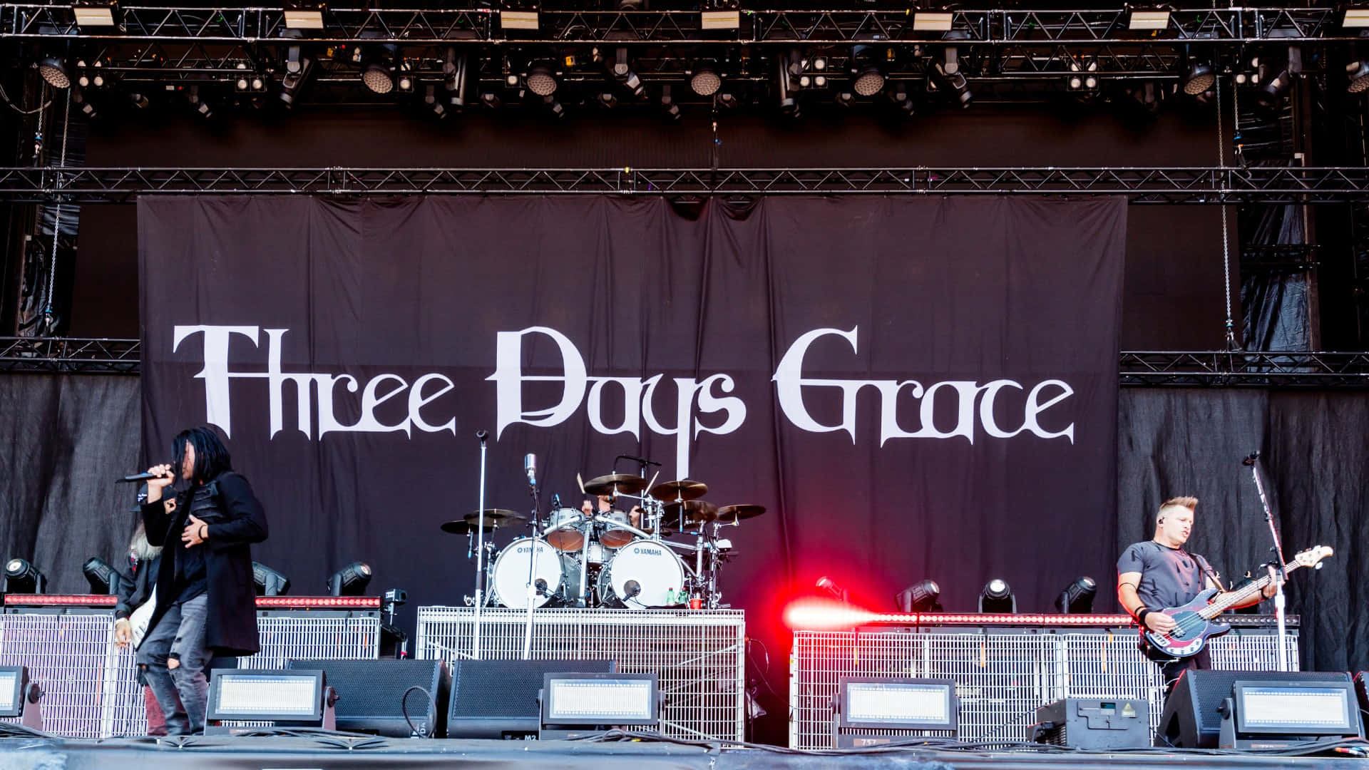  壁紙 — Three Days Grace 樂隊在舞台上現場表演，鼓手在鼓組後面，結他手在明亮的舞台燈光下演奏。