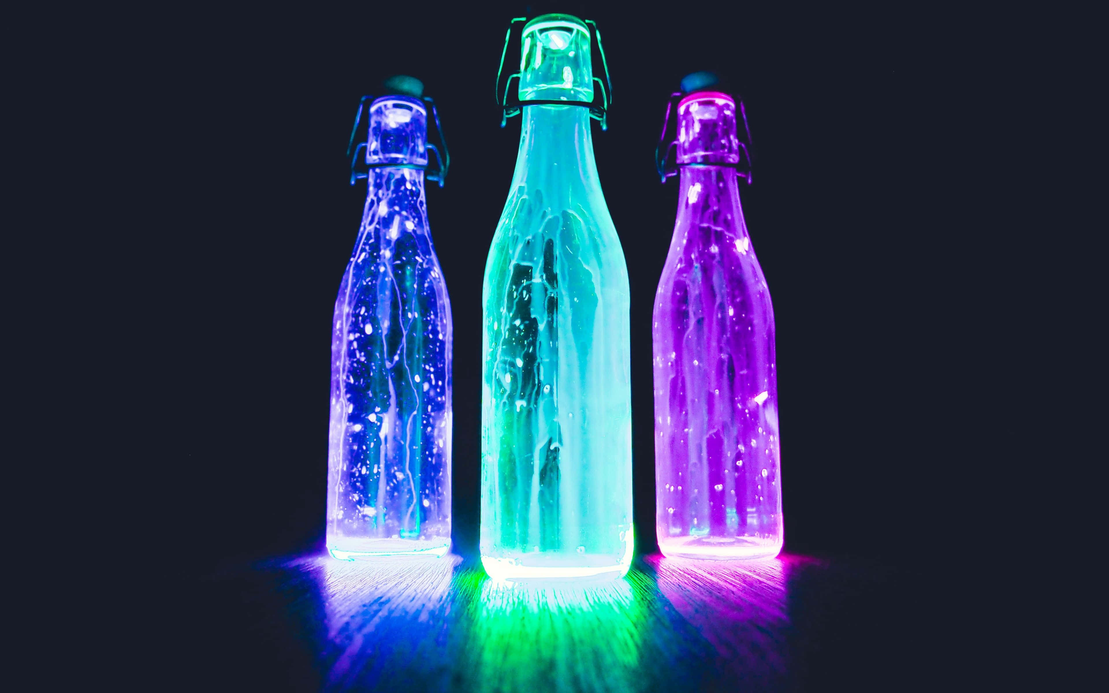 Neon Nature 桌布 壁紙 — 三個發光的玻璃瓶，帶有翻蓋，在黑暗背景下發出鮮豔的藍色、綠色和紫色光芒。