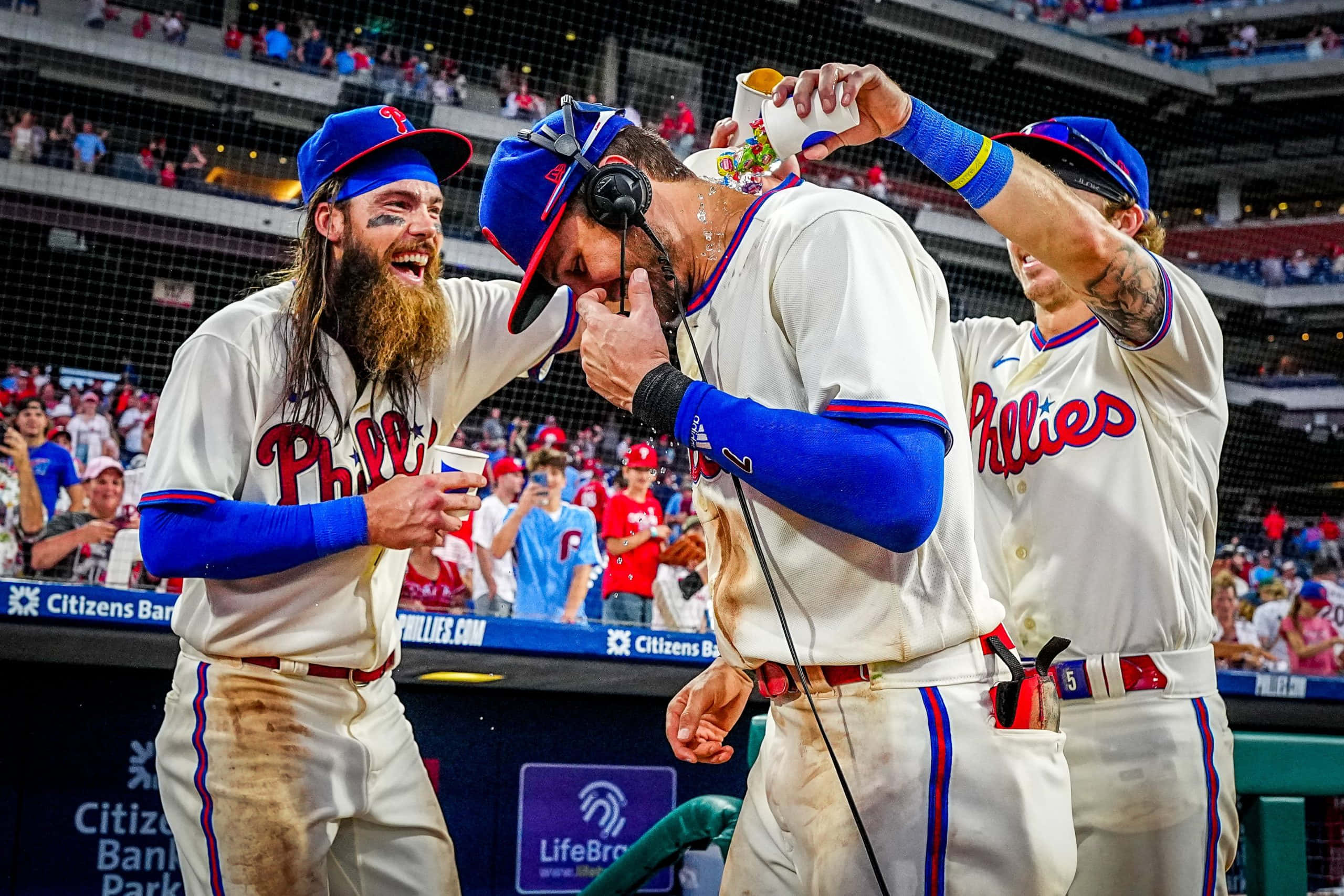 Trea Turner Phillies 桌布 壁紙 — 三名費城費城人棒球運動員在市民銀行公園球場以泥濘的球衣和慶祝飲料慶祝。