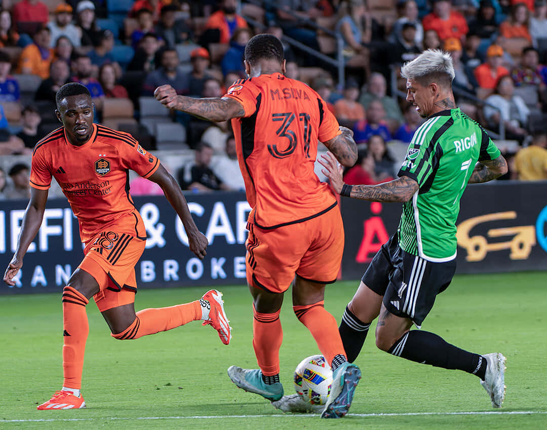  壁紙 — 三名足球運動員在體育場燈光下，於充滿活力的綠色場地上激烈爭球。
