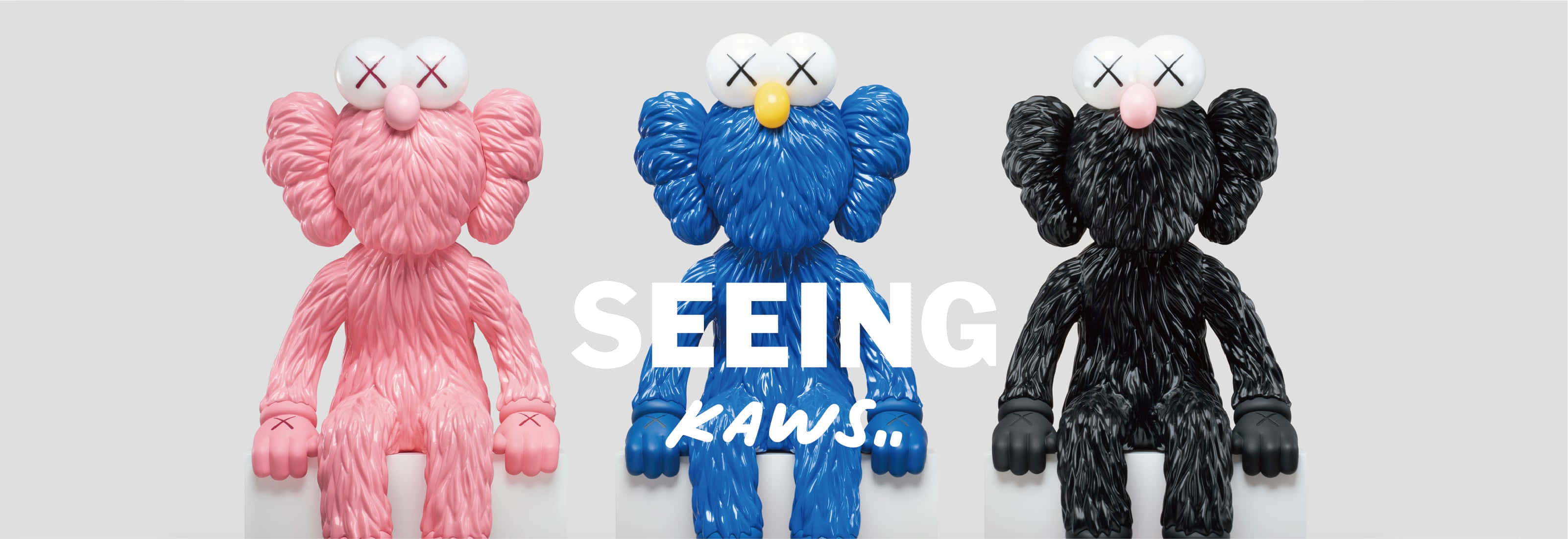 KAWS 的創意與色彩繽紛藝術作品 壁紙 — 三個帶有紋理的KAWS毛絨公仔，分別是粉紅色、藍色和黑色，並排站在純灰色背景上，配有粗體白色文字。