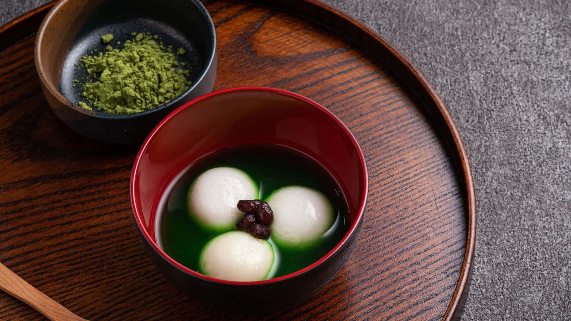  壁紙 — 三個白色麻糬漂浮在鮮綠色的抹茶中，旁邊放著一碗抹茶粉在木托盤上。