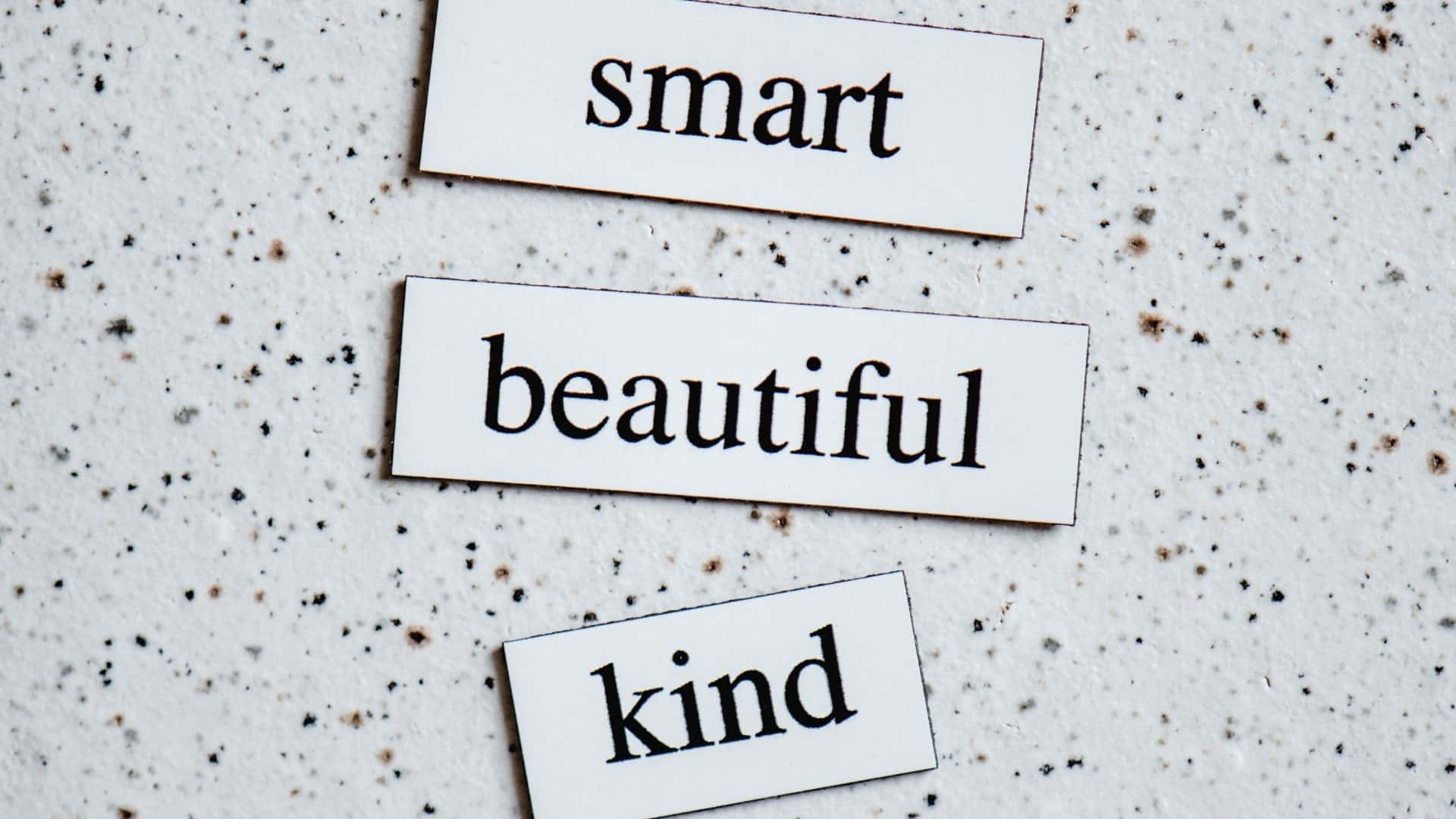  壁紙 — 三個白色長方形標籤，上面有黑色文字寫著 smart beautiful kind，以對角線方式排列在帶有斑點的灰色表面上。