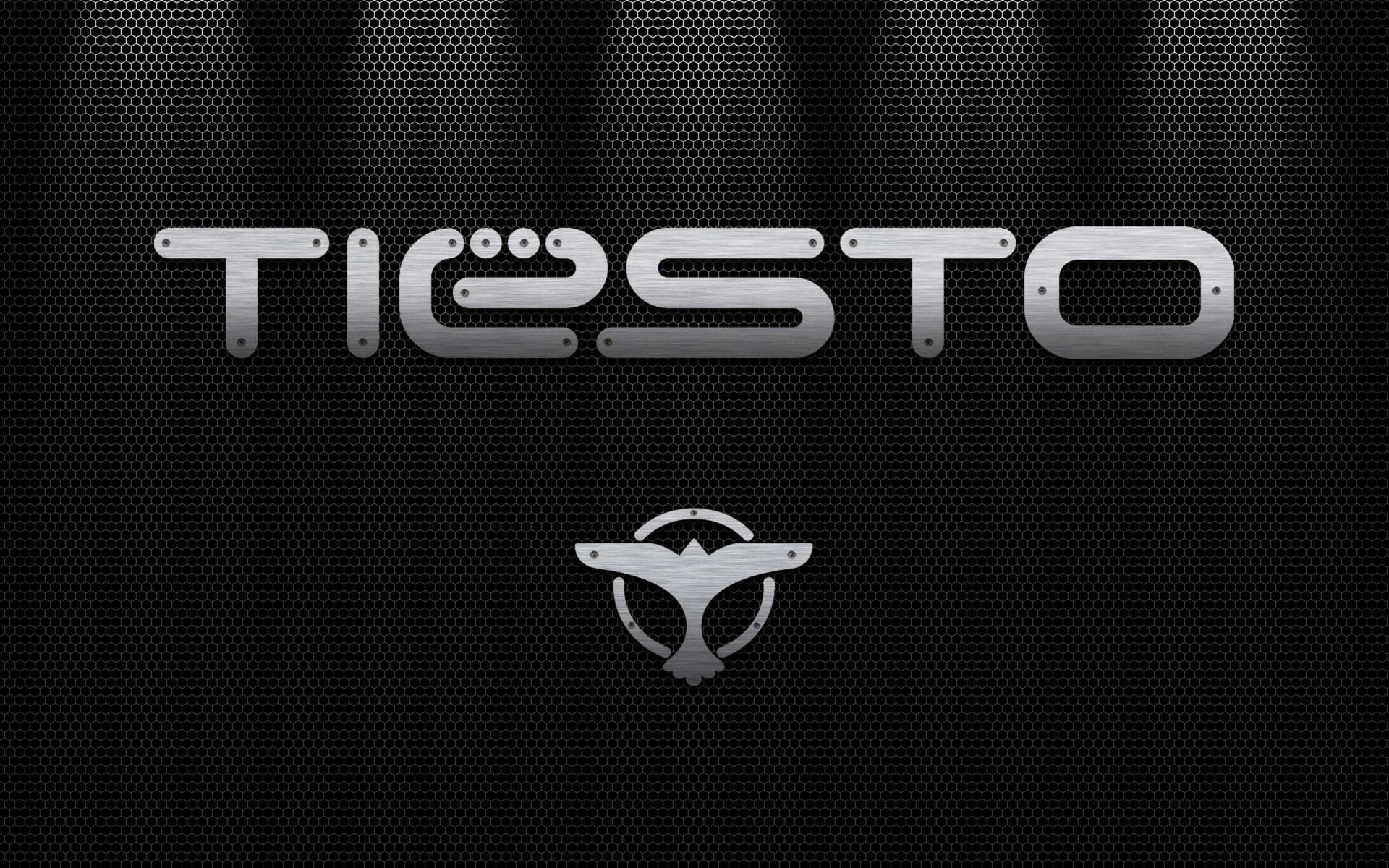 Tiesto 標誌，帶有翼形徽章，位於穿孔金屬背景上，配有聚光燈。