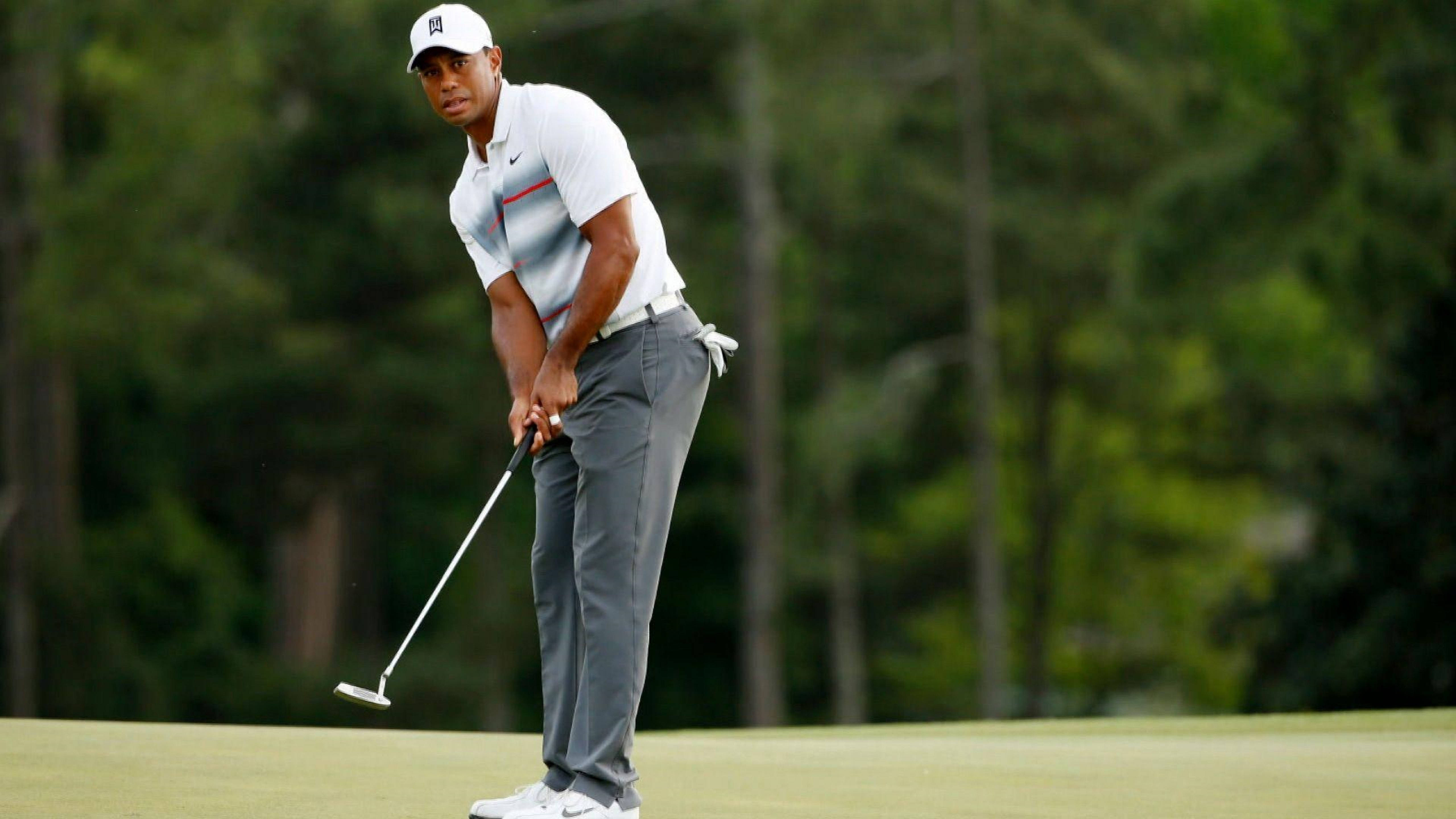 Tiger Woods 擊球姿勢 壁紙 — 老虎活士在陽光明媚、綠樹成蔭的高爾夫果嶺上專注地瞄準推桿。